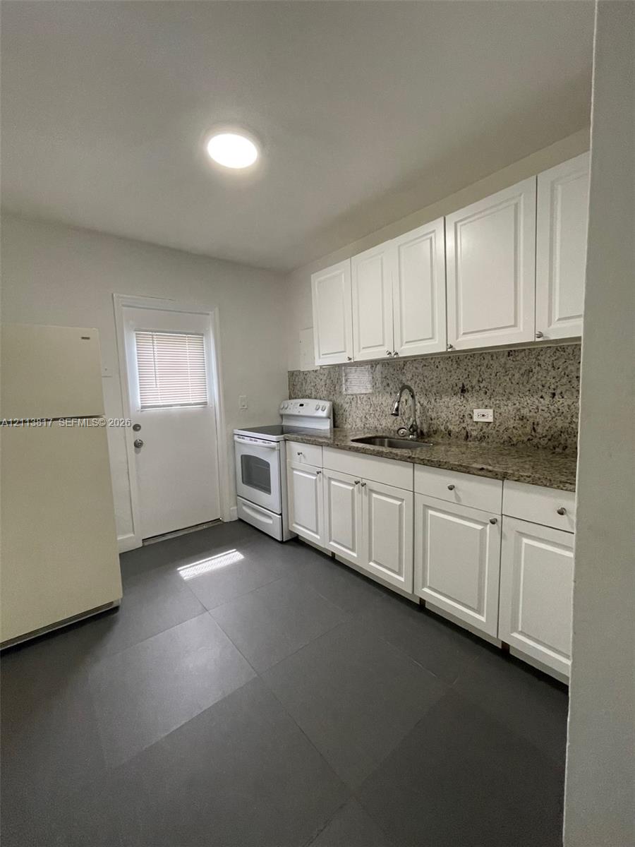 Kitchen featuring white cabinetry, stone-surface countertops, tile flooring, and stainless steel hardware