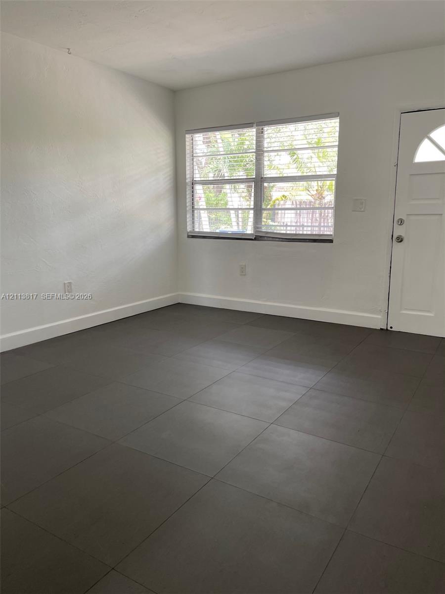 Neutral-toned tile flooring, white wall finish, multi-pane window, and exterior door with a crescent-shaped glass inset