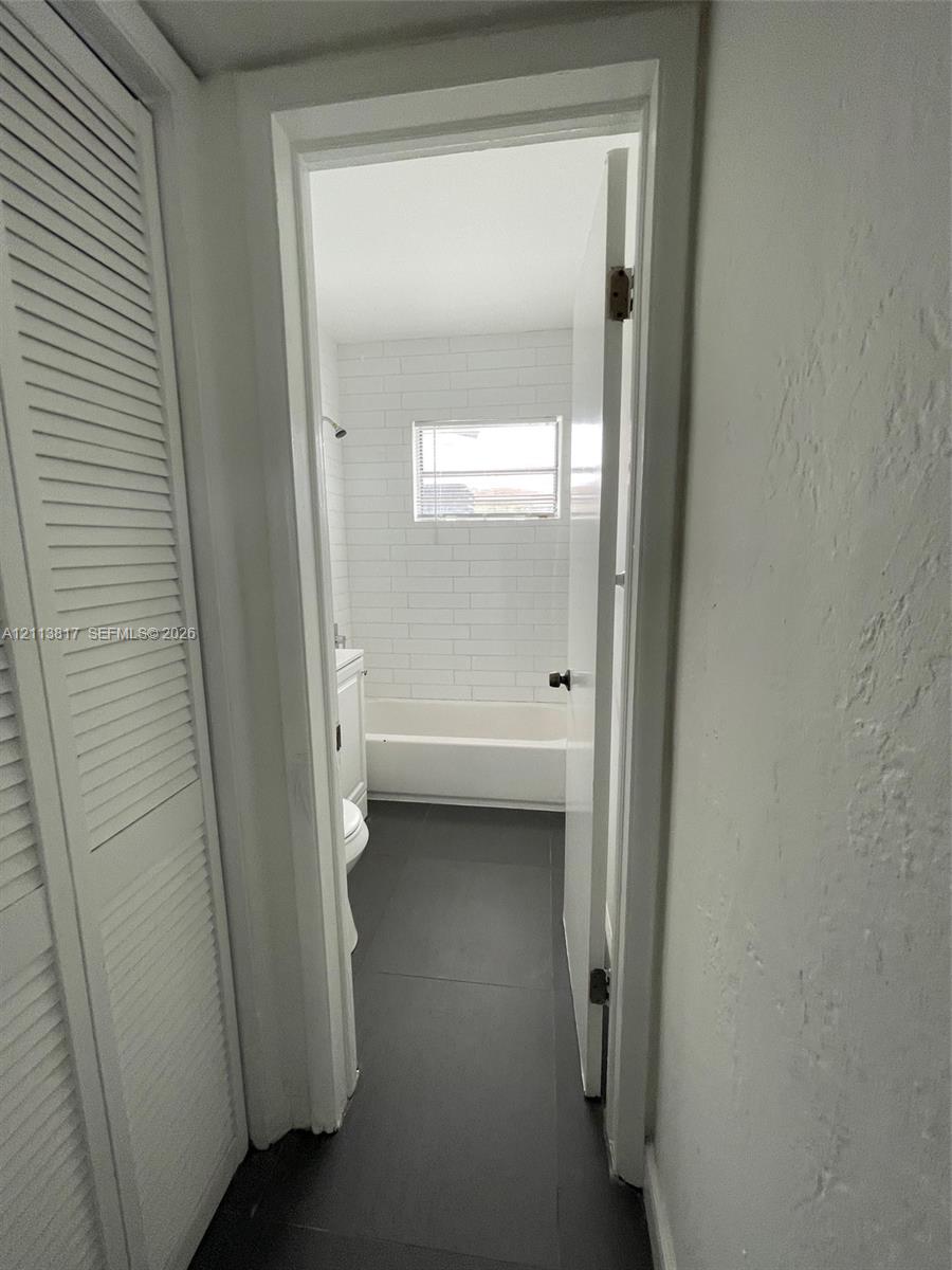 Bathroom featuring large-format dark floor tile, white subway tile shower surround, and louvered-style closet doors