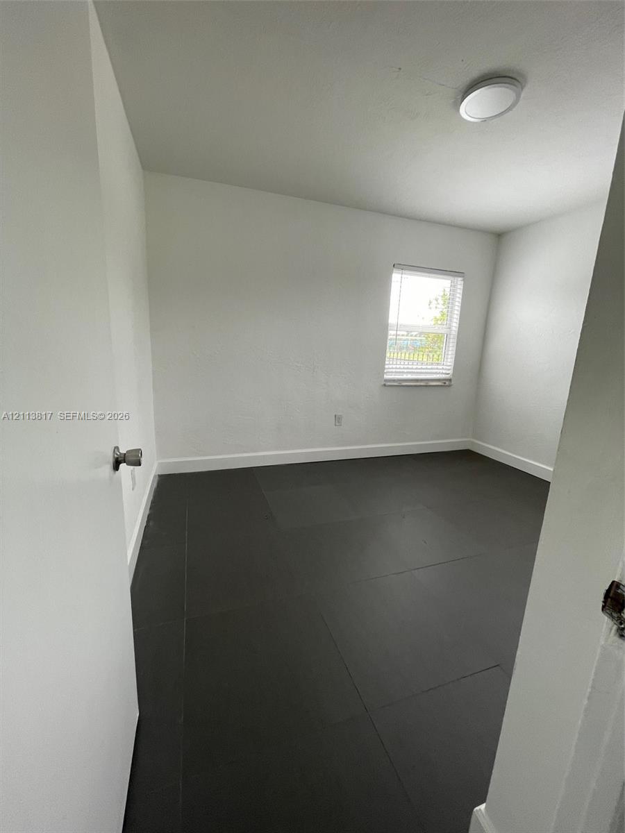 Neutral wall tones, dark tile flooring, a single-pane window, and a flush-mount overhead light fixture