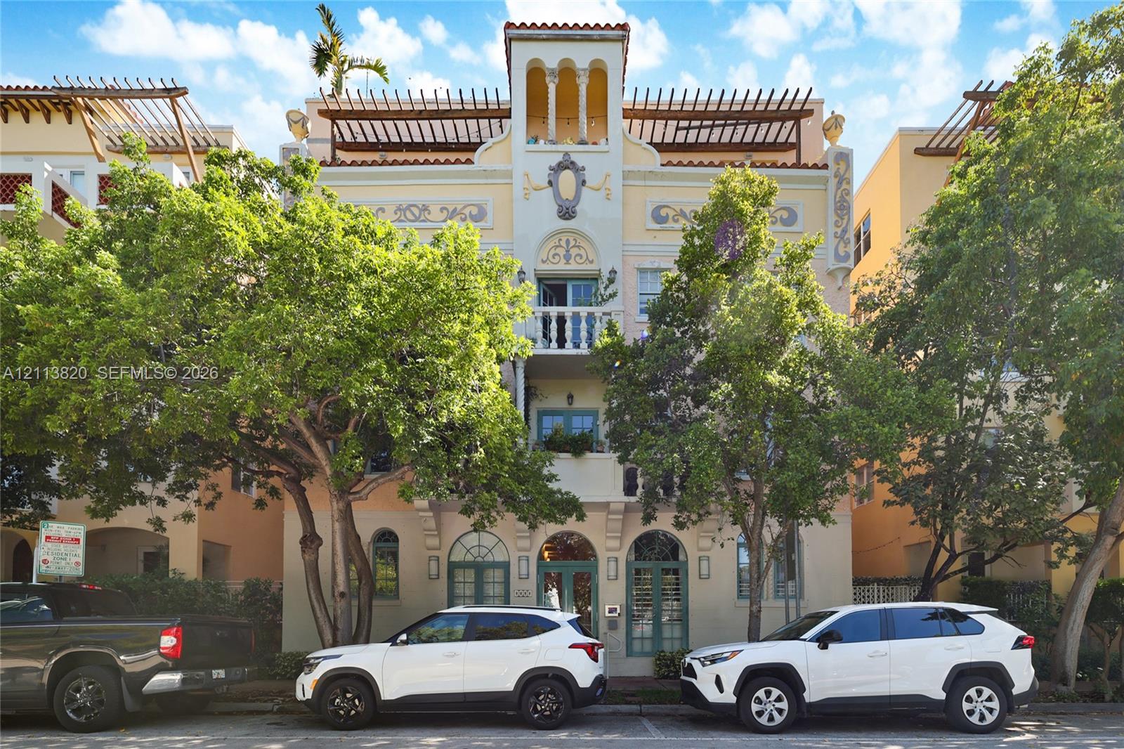 Mediterranean-inspired exterior featuring stucco facade, arched multi-pane glass entry doors, second-story balcony with decorative balustrade, and symmetrical arched window detailing