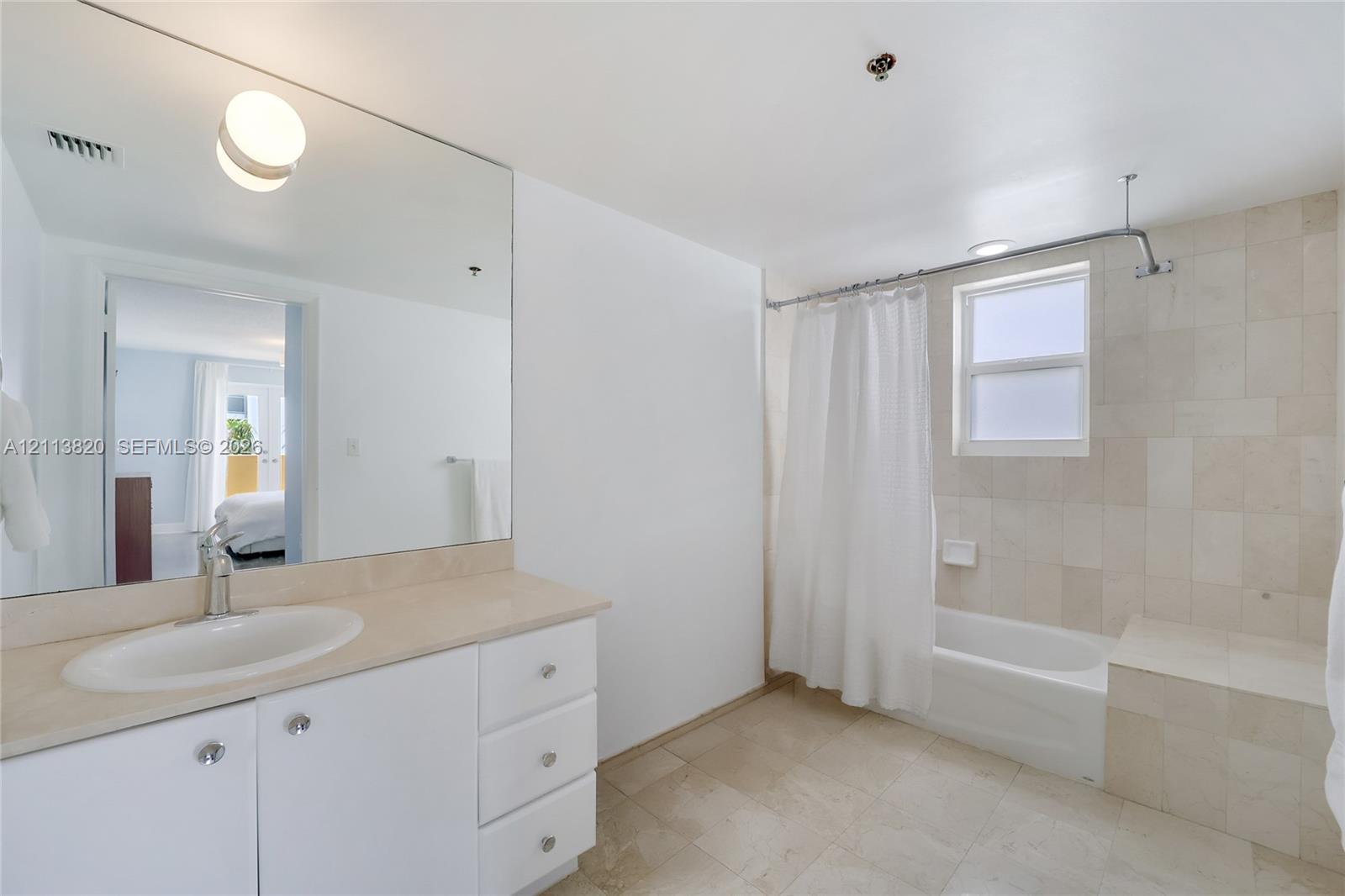 Bathroom featuring white cabinetry, stone-surface countertop with an integrated oval sink, large wall-mounted mirror, and tile-surround bathtub with an integrated seating ledge