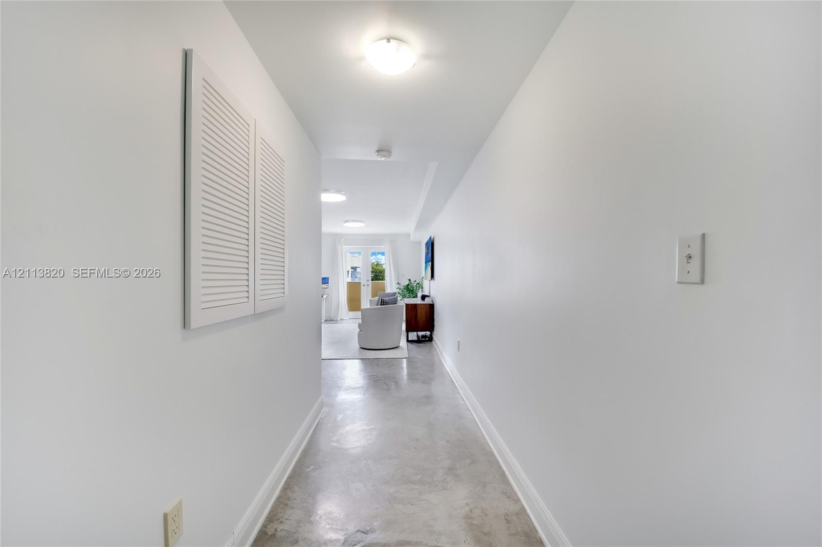 Hallway featuring polished concrete flooring, white walls, louvered closet doors, and flush-mount ceiling lighting Hallway featuring polished concrete flooring, white walls, louvered closet doors, and flush-mount ceiling lighting