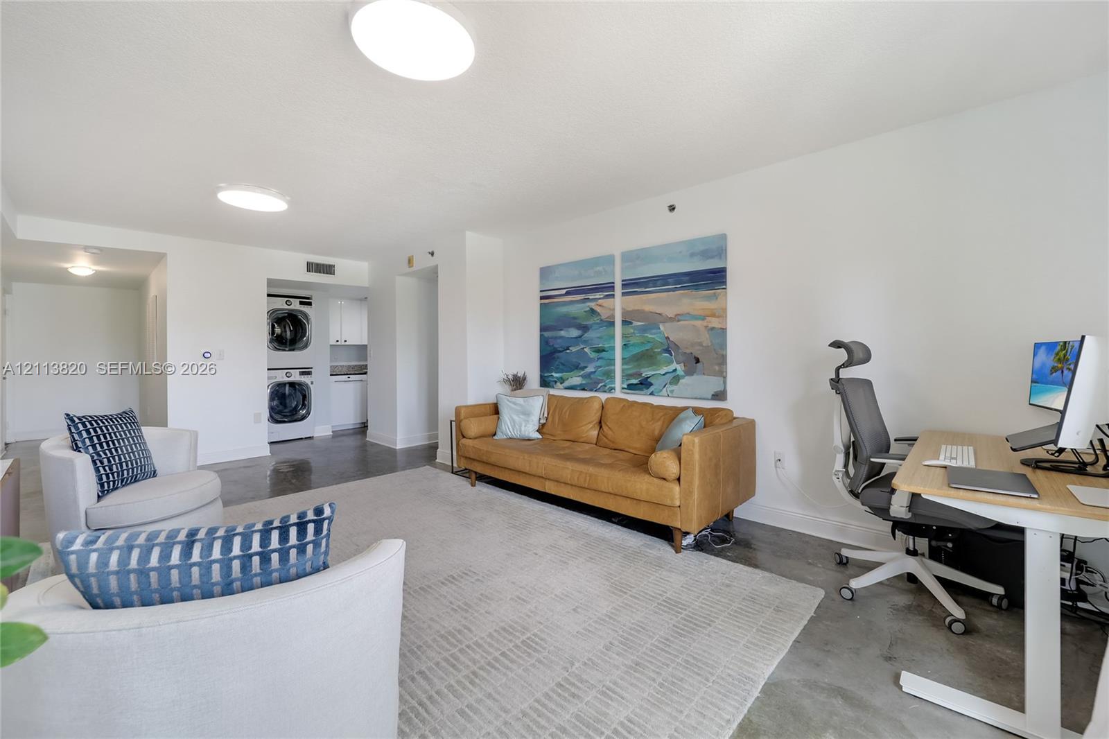 Open-concept interior featuring polished concrete flooring, recessed lighting, and a dedicated laundry area with stacked washer and dryer unit Open-concept interior featuring polished concrete flooring, recessed lighting, and a dedicated laundry area with stacked washer and dryer unit