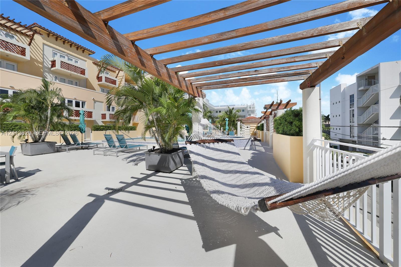 Outdoor terrace featuring a wooden pergola, concrete flooring, perimeter white metal railings, and integrated masonry planters