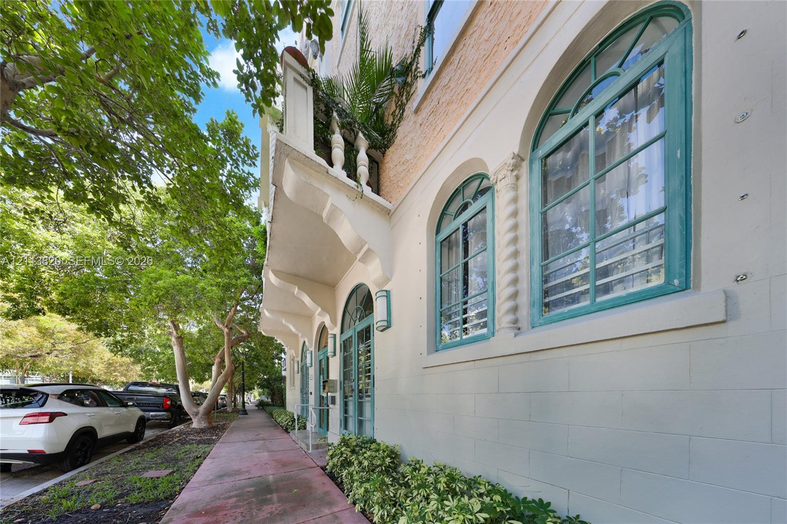 Entrance featuring arched glass-paneled double doors, flanking arched windows with teal frames, decorative corbel accents, and wall-mounted exterior sconces
