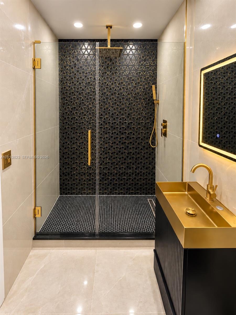 Walk-in shower featuring gold-tone fixtures, a rainfall showerhead, and geometric patterned wall tile