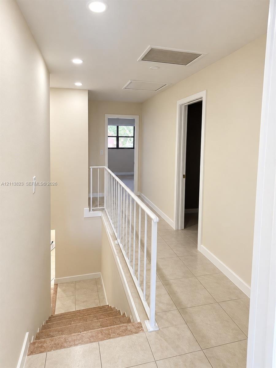 Neutral tile flooring, white metal railing, and recessed ceiling lighting
