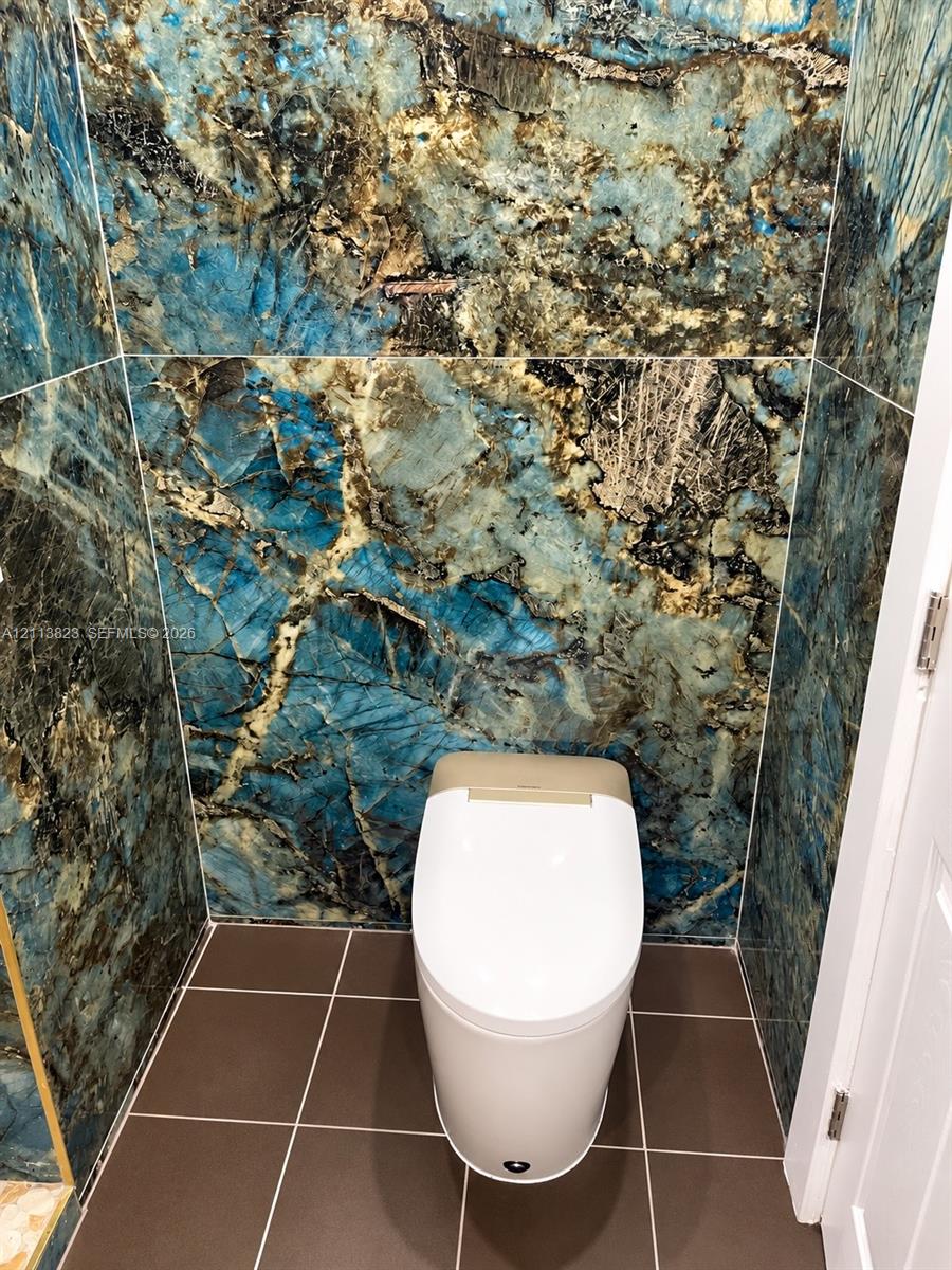 Full-height stone wall cladding with polished finish, large-format matte floor tile, and modern one-piece toilet
