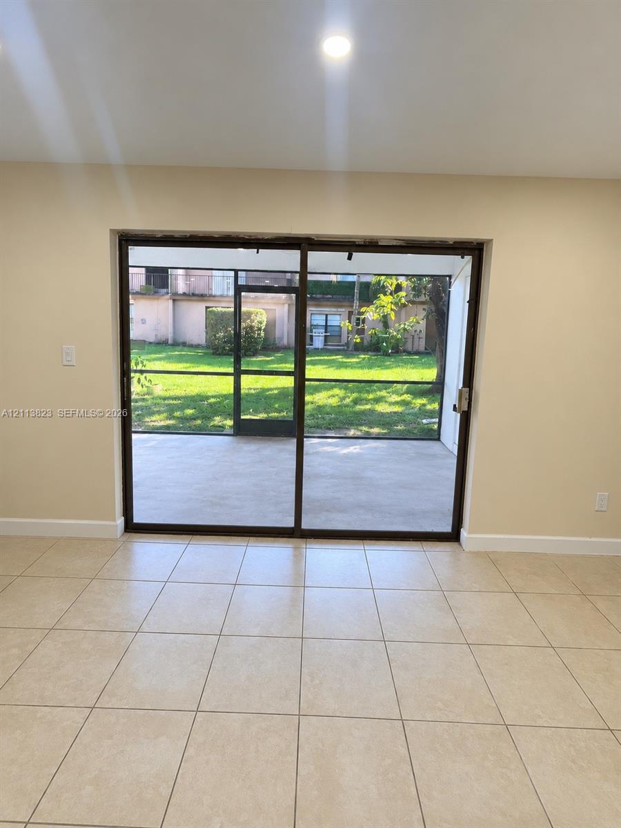 Large-format sliding glass doors featuring dark-finish frames, neutral ceramic tile flooring, recessed ceiling lighting, and a screened-in lanai with an expansive lawn area