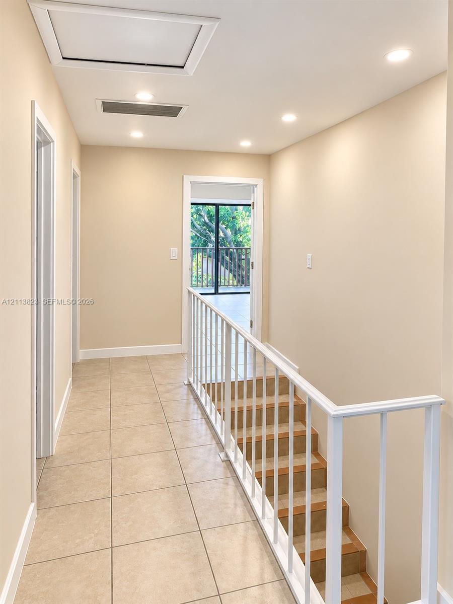 Neutral-toned tile flooring, recessed ceiling lighting, and a white metal staircase railing