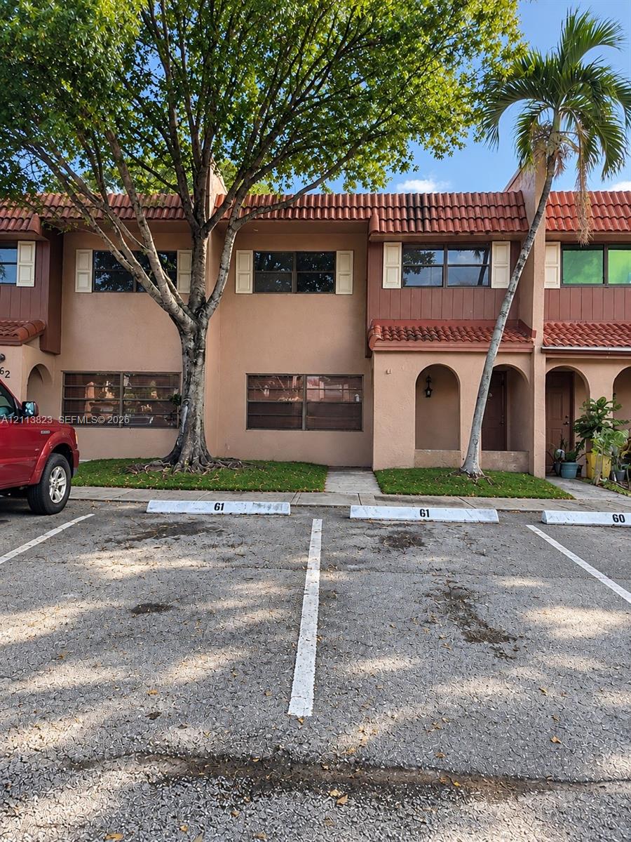 Stucco exterior featuring mission-style clay tile roofing, arched entryway, horizontal window shutters, and designated off-street parking