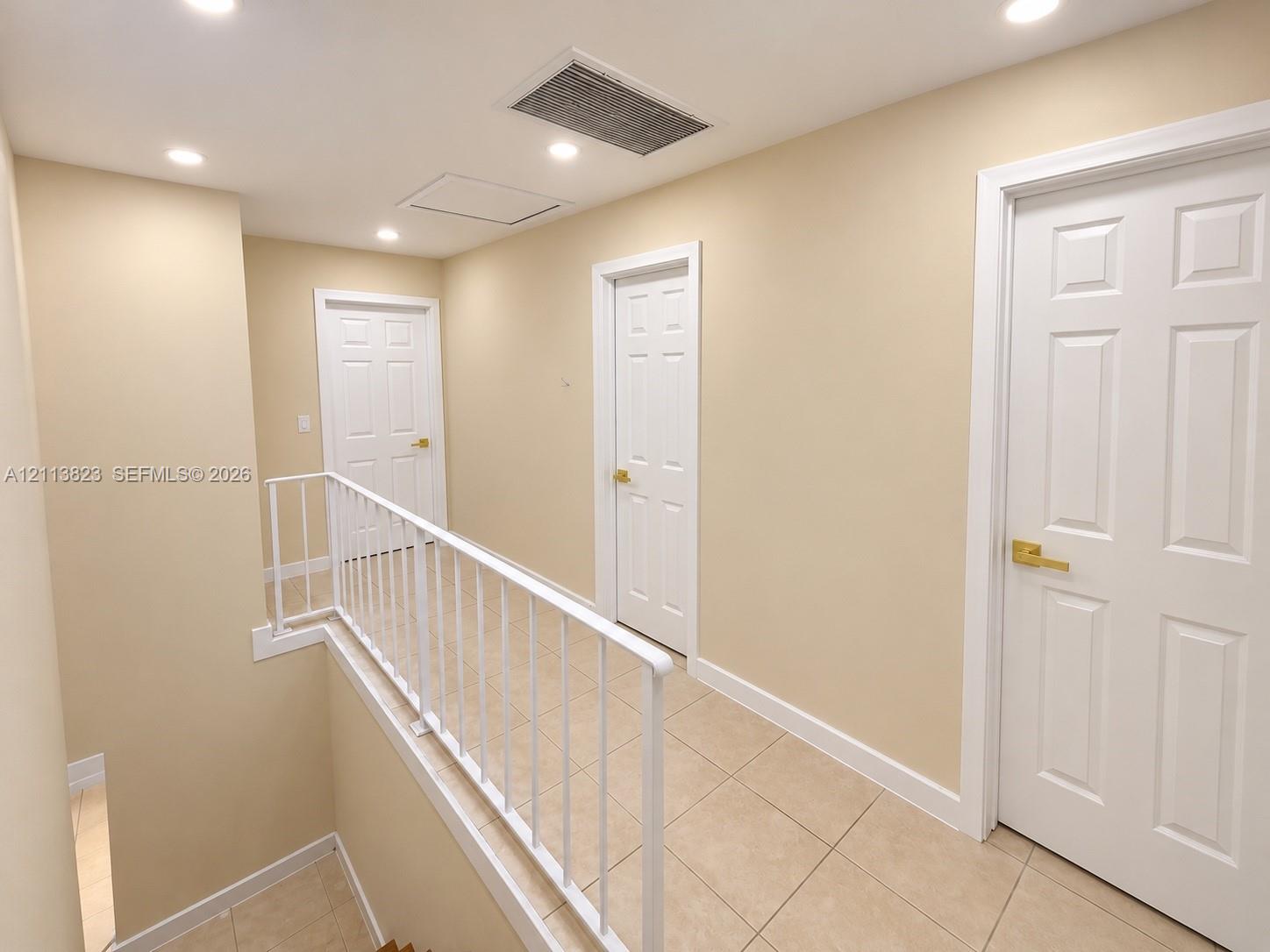 Interior hallway featuring tile flooring, white six-panel doors with metallic hardware, recessed lighting, and a white metal railing