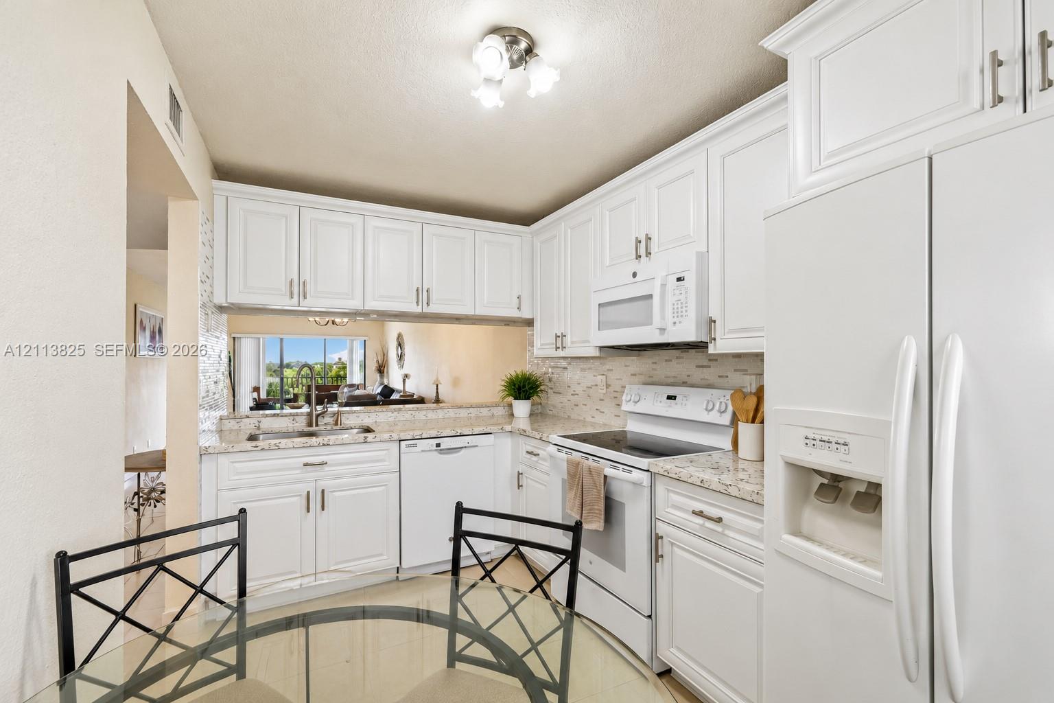 Kitchen featuring white shaker-style cabinetry, stone-finish countertops, tile backsplash, built-in white appliances, and a double-basin stainless steel sink