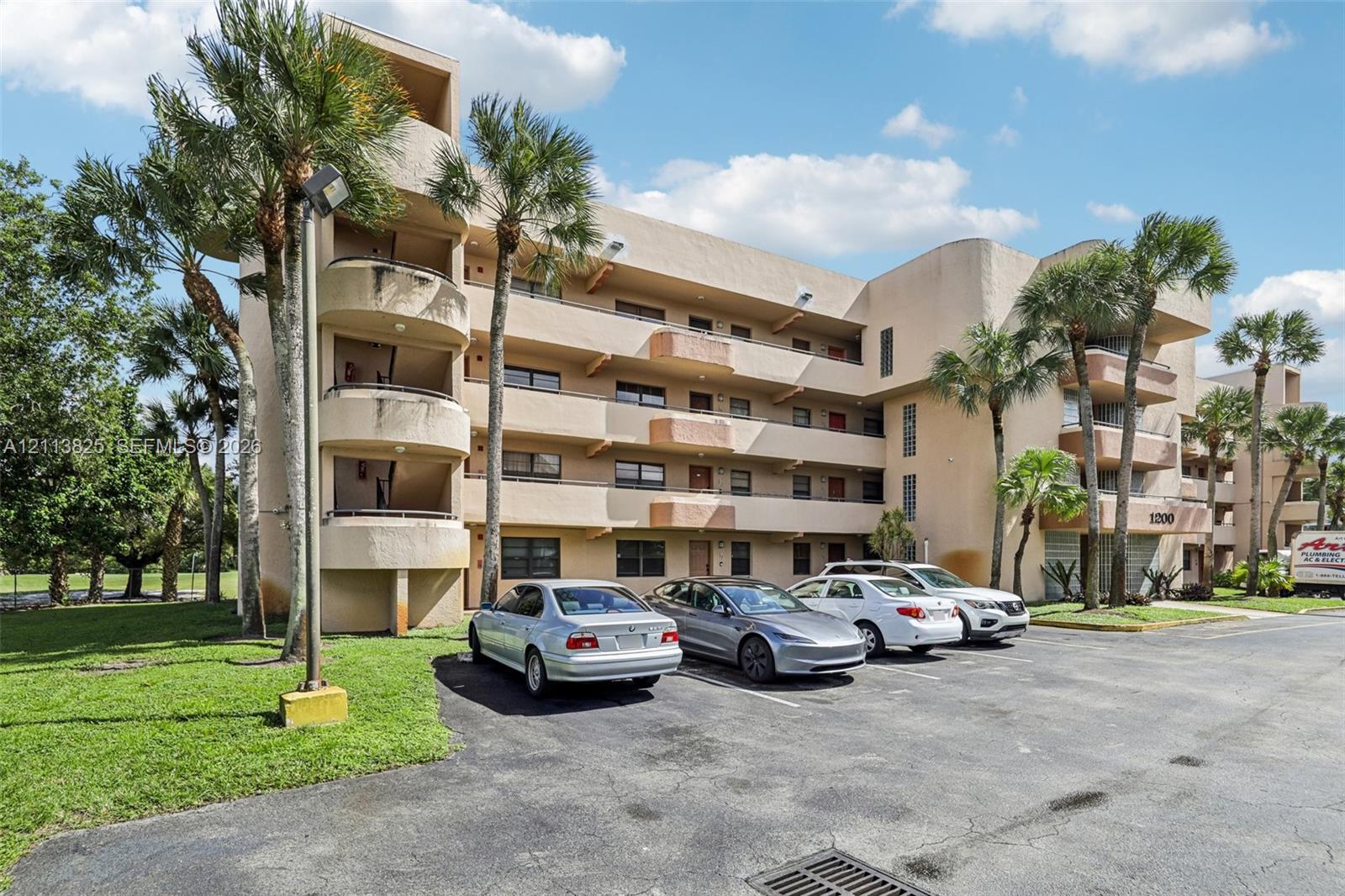 Multi-story residential building featuring stucco exterior, private curved balconies, and mature palm tree landscaping