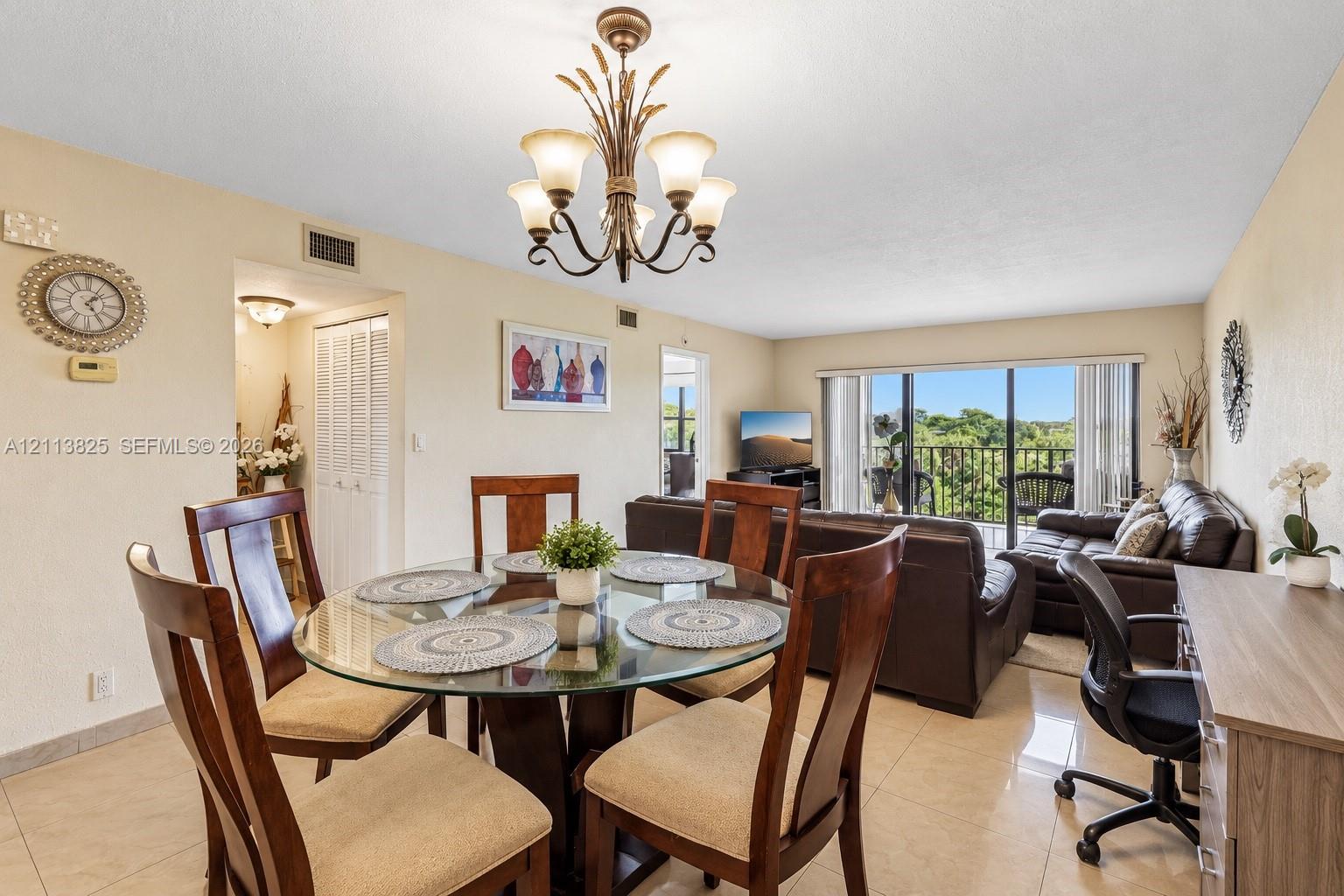 Open-concept floor plan featuring large-format tile flooring, a multi-arm decorative chandelier, and sliding glass doors with access to an exterior balcony
