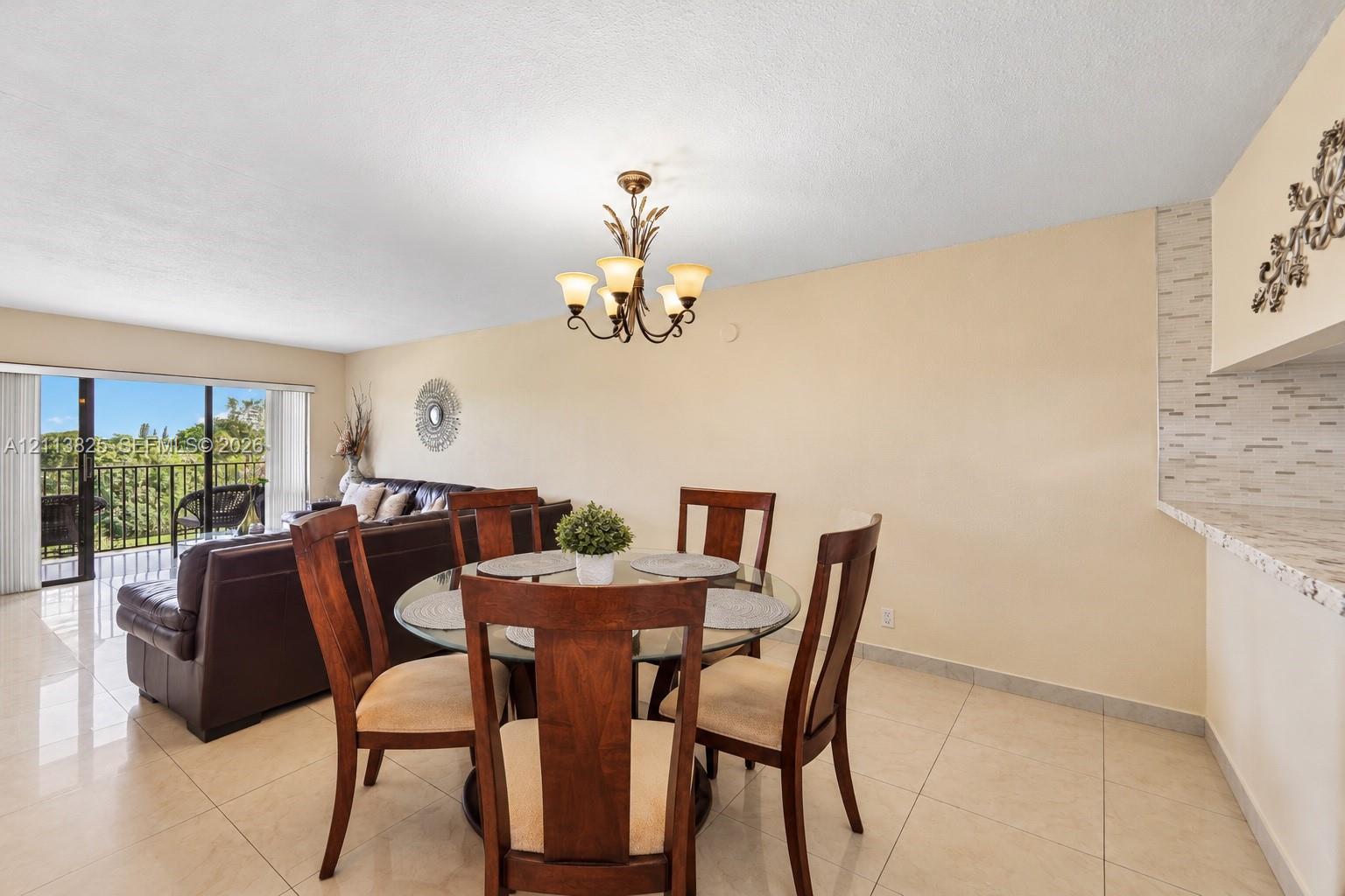 Open-concept area featuring tile flooring, a multi-arm chandelier, and a breakfast bar with stone-finish surfacing and decorative tile backsplash