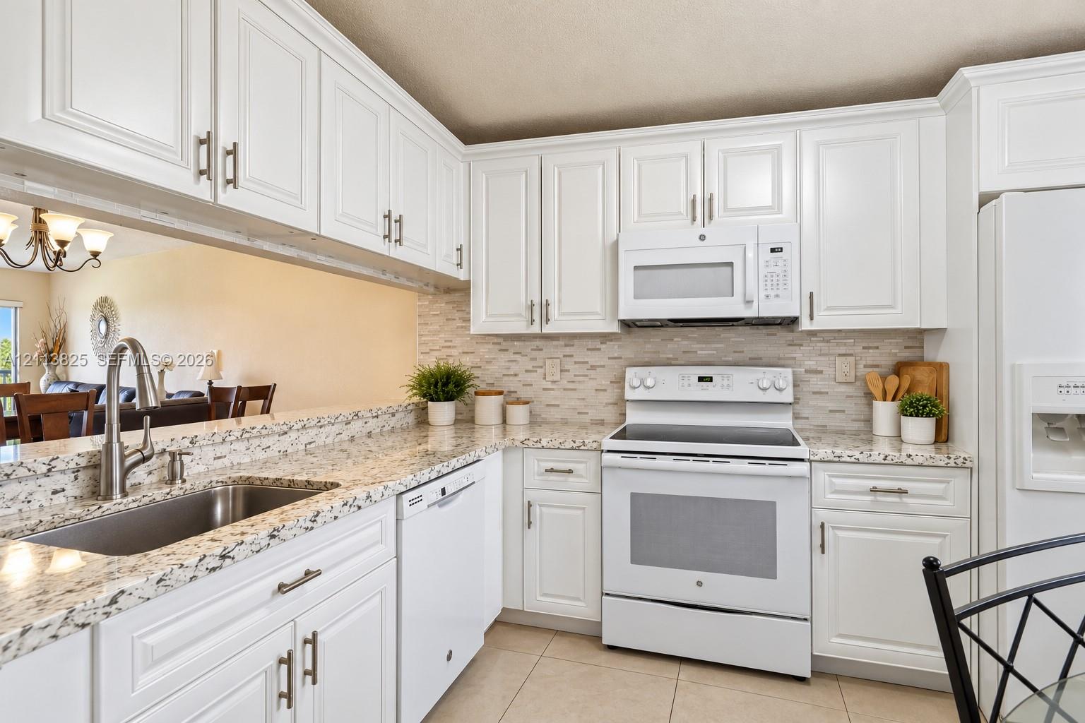 Kitchen featuring white shaker-style cabinetry, speckled stone countertops, a subway tile backsplash, and stainless steel undermount sink