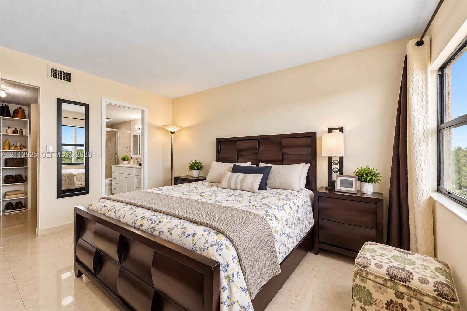 Spacious room featuring neutral tile flooring, a wall-mounted rectangular mirror with a dark frame, and a walk-in storage area with built-in shelving
