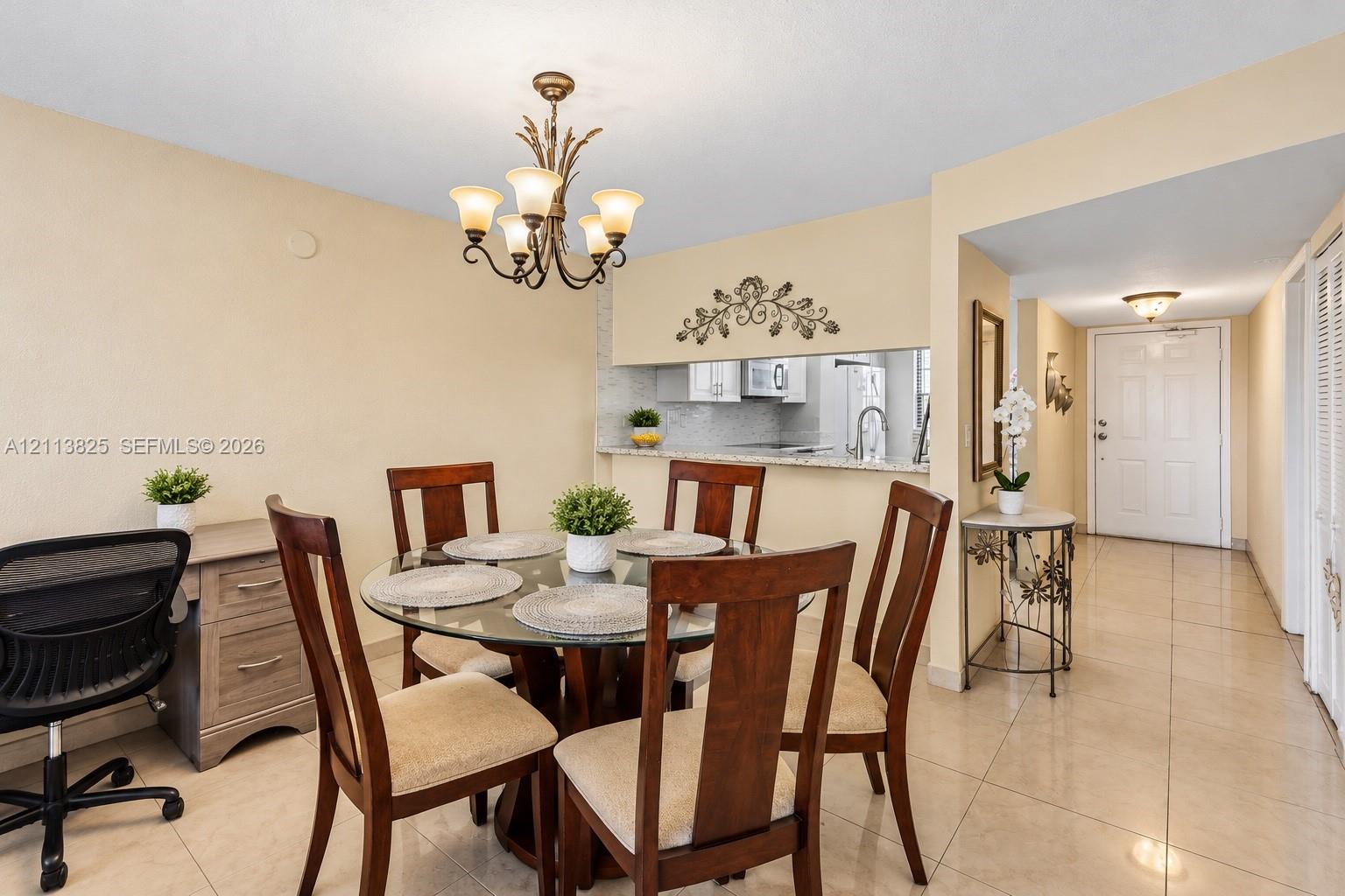 Neutral tile flooring, decorative multi-arm chandelier, and open-concept pass-through window with solid-surface countertop