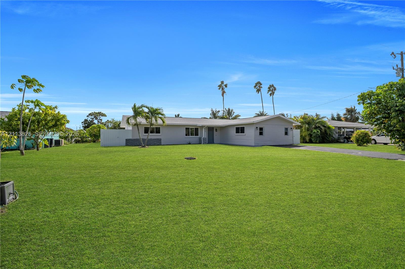 Single-story residence featuring a light-toned exterior, a spacious front lawn, mature palm trees, and an attached carport