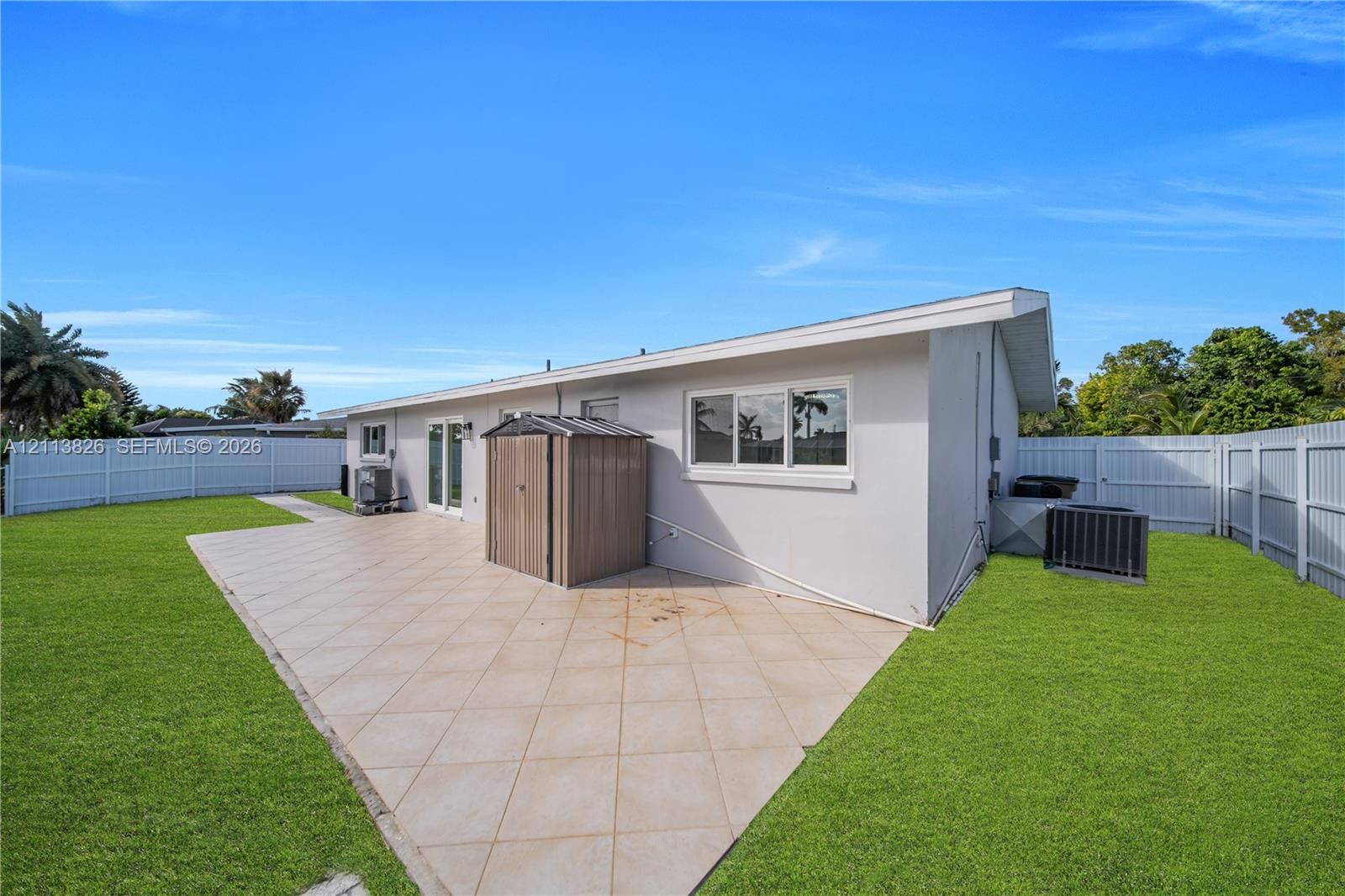 Rear exterior featuring a spacious tiled patio, expansive lawn, and full-perimeter vinyl privacy fencing