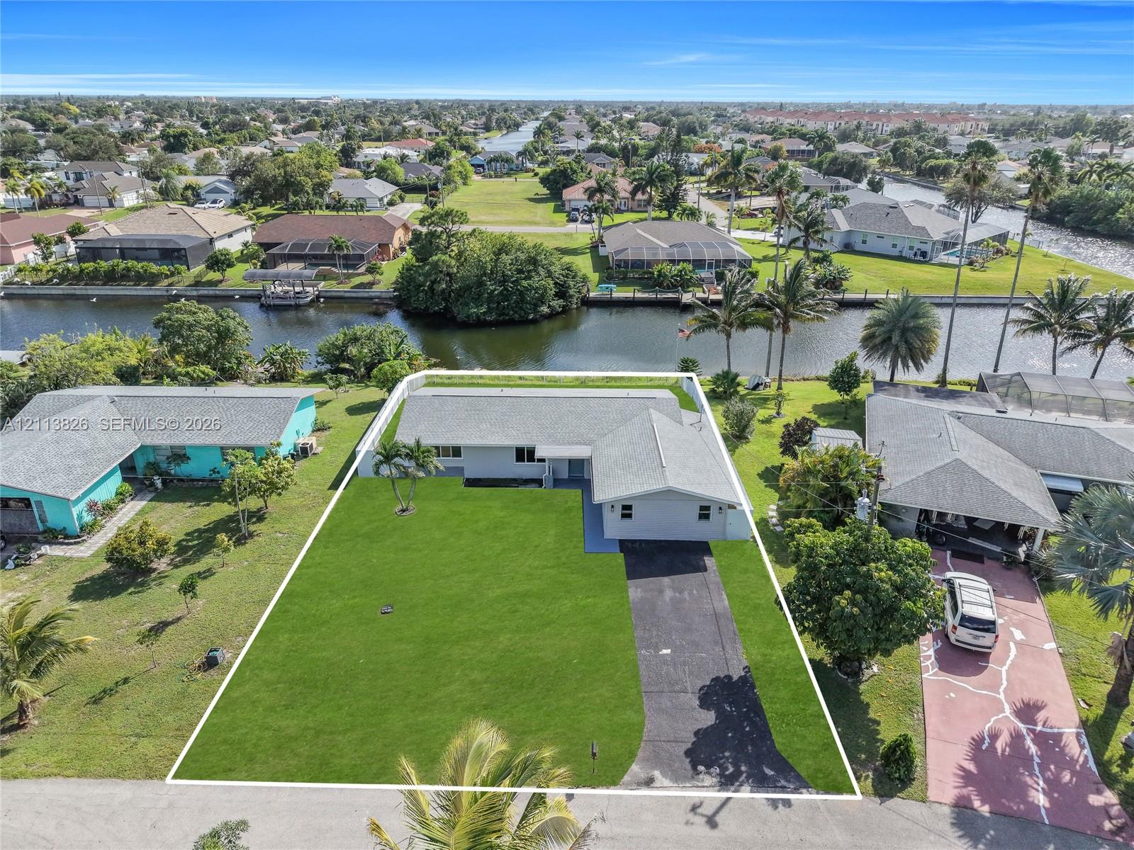Single-story residence featuring a shingled roof, asphalt driveway, manicured lawn, and waterfront access Single-story residence featuring a shingled roof, asphalt driveway, manicured lawn, and waterfront access