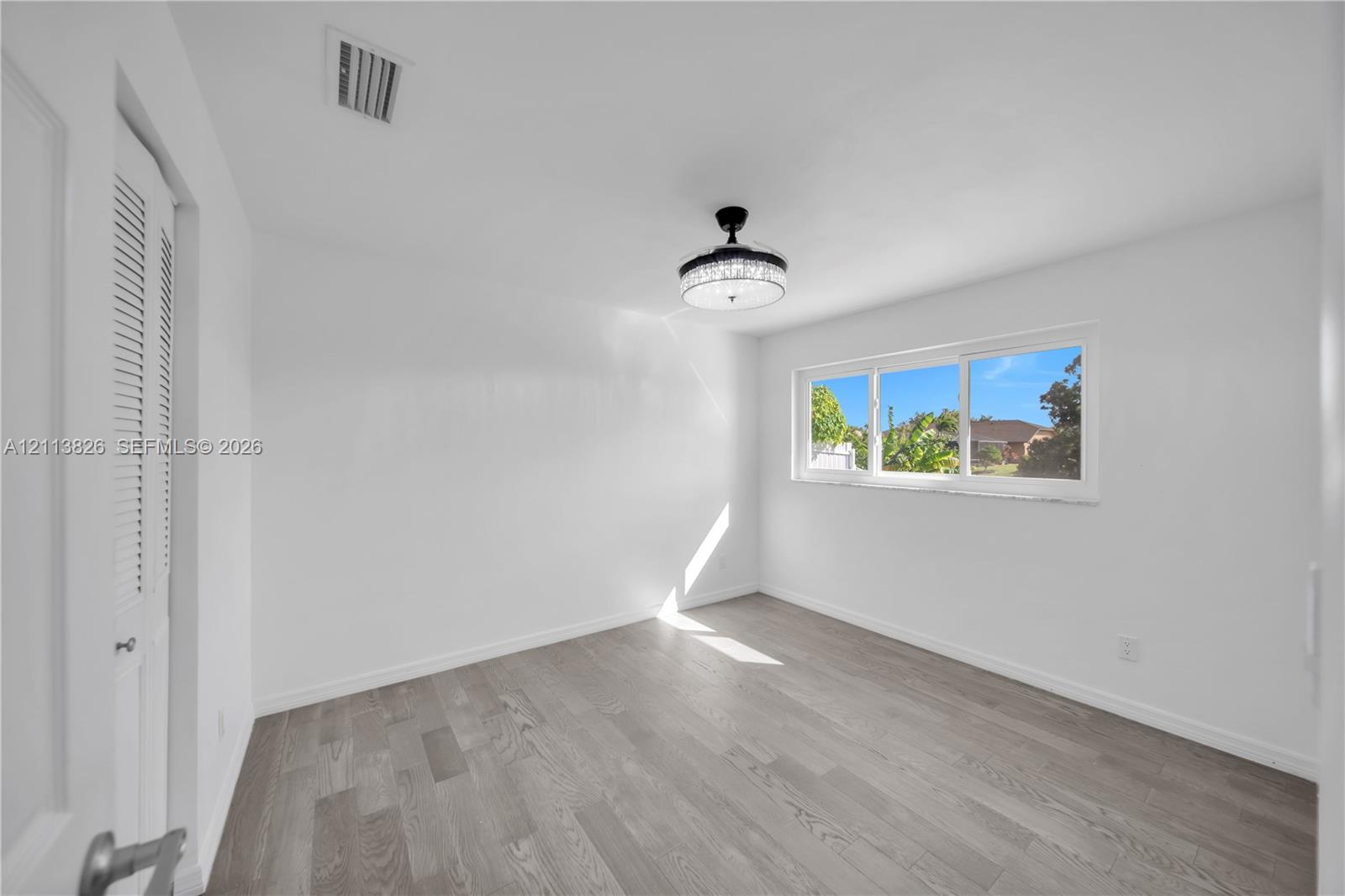 Room featuring wood-finish flooring, a ceiling-mounted light fixture, white walls, a horizontal sliding window, and louvered closet doors