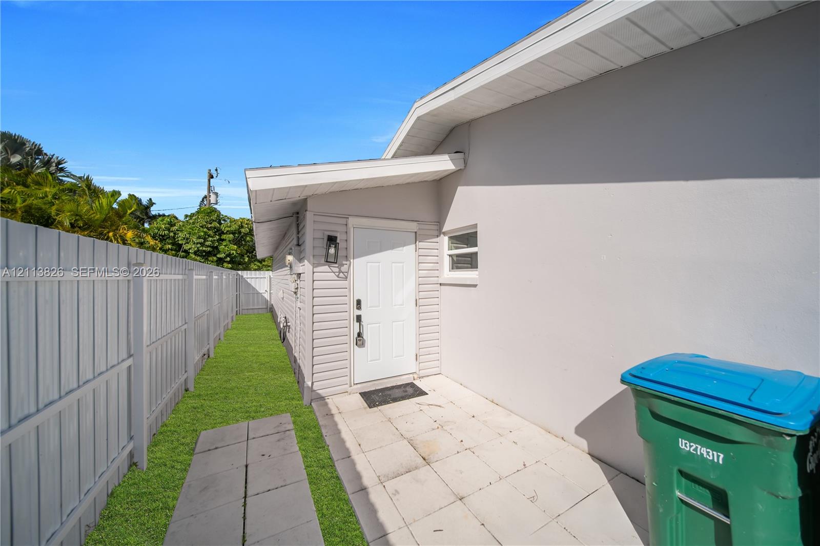 Exterior side yard featuring white vinyl privacy fencing, paved concrete walkway, and smooth stucco finish