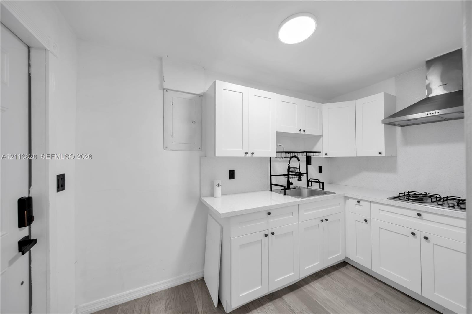 Kitchen featuring white shaker-style cabinetry, solid-surface countertops, stainless steel gas cooktop, stainless steel range hood, and wood-finish flooring