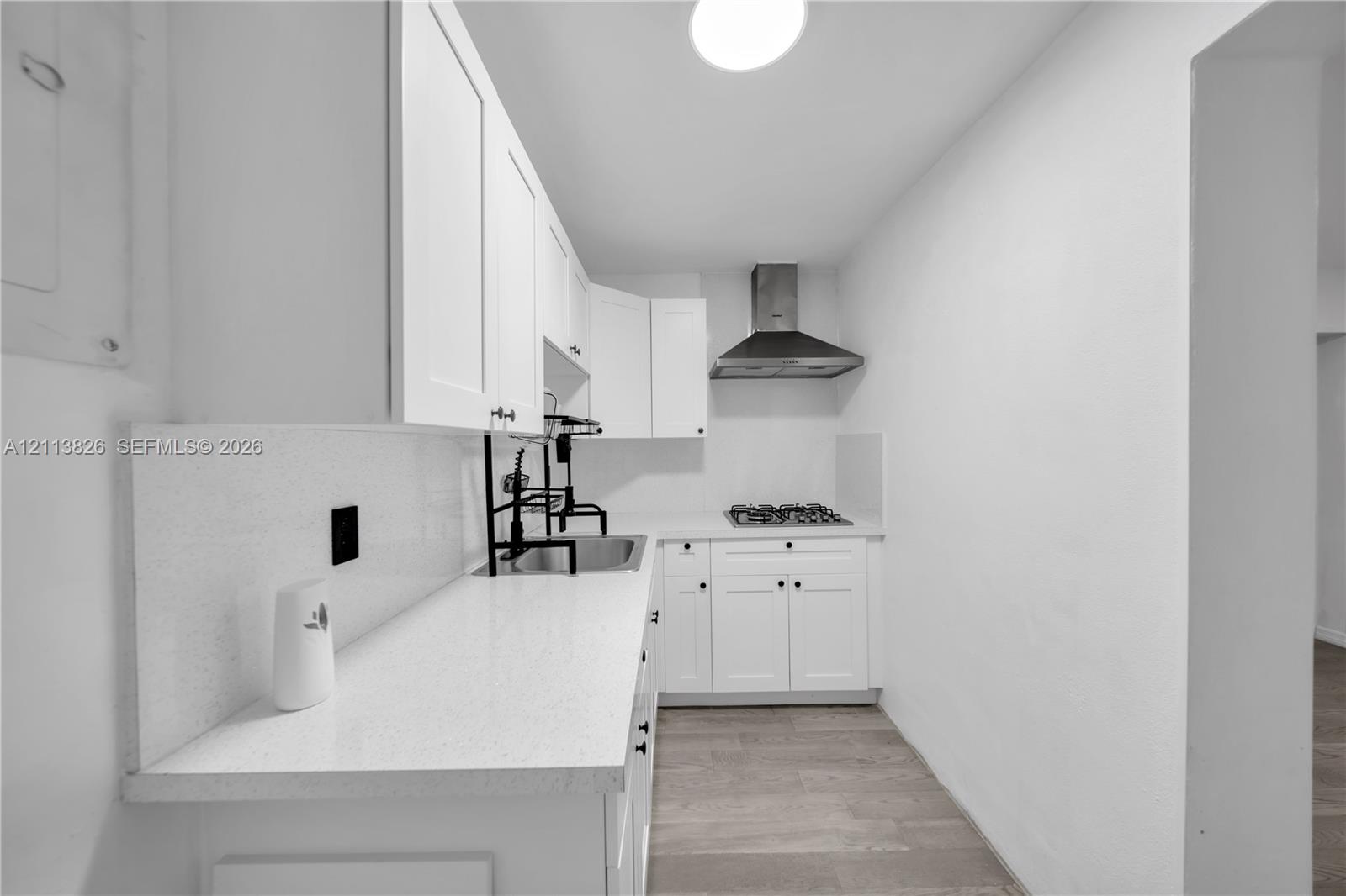 Kitchen featuring white cabinetry, solid-surface countertops, wood-finish flooring, a stainless steel range hood, and a gas cooktop