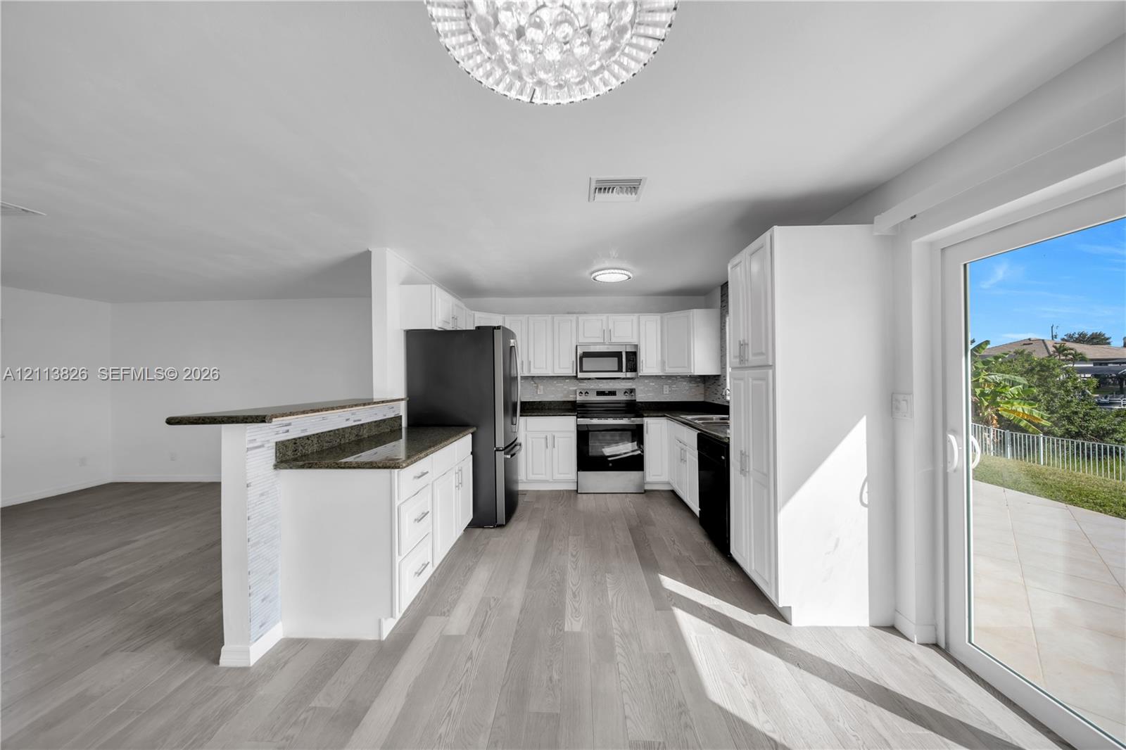 Kitchen featuring white cabinetry, dark stone-finish countertops, stainless steel appliances, wood-finish flooring, and glass sliding doors