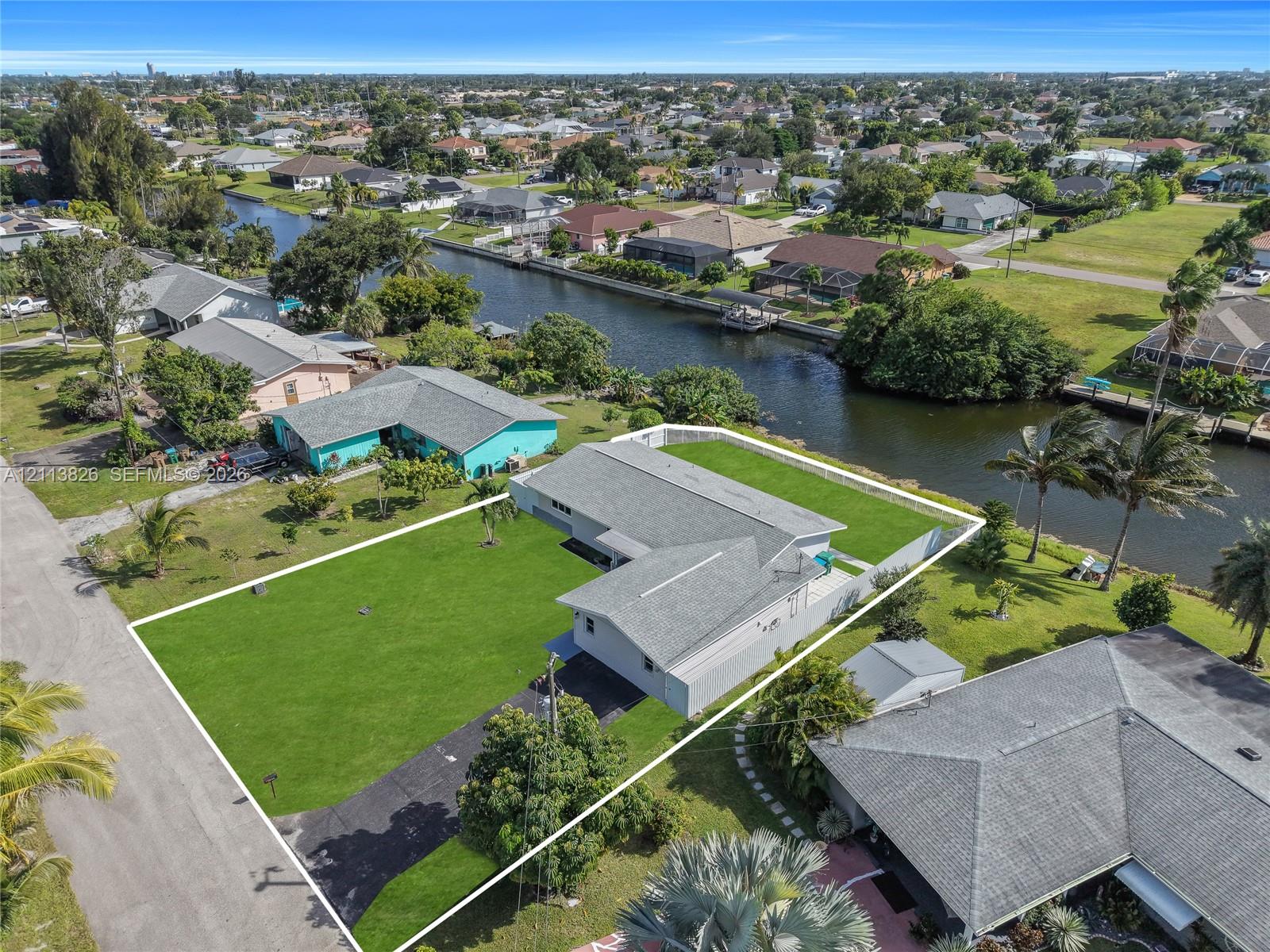 Waterfront property featuring a canal-side lot, expansive grass lawn, asphalt driveway, and shingle roof