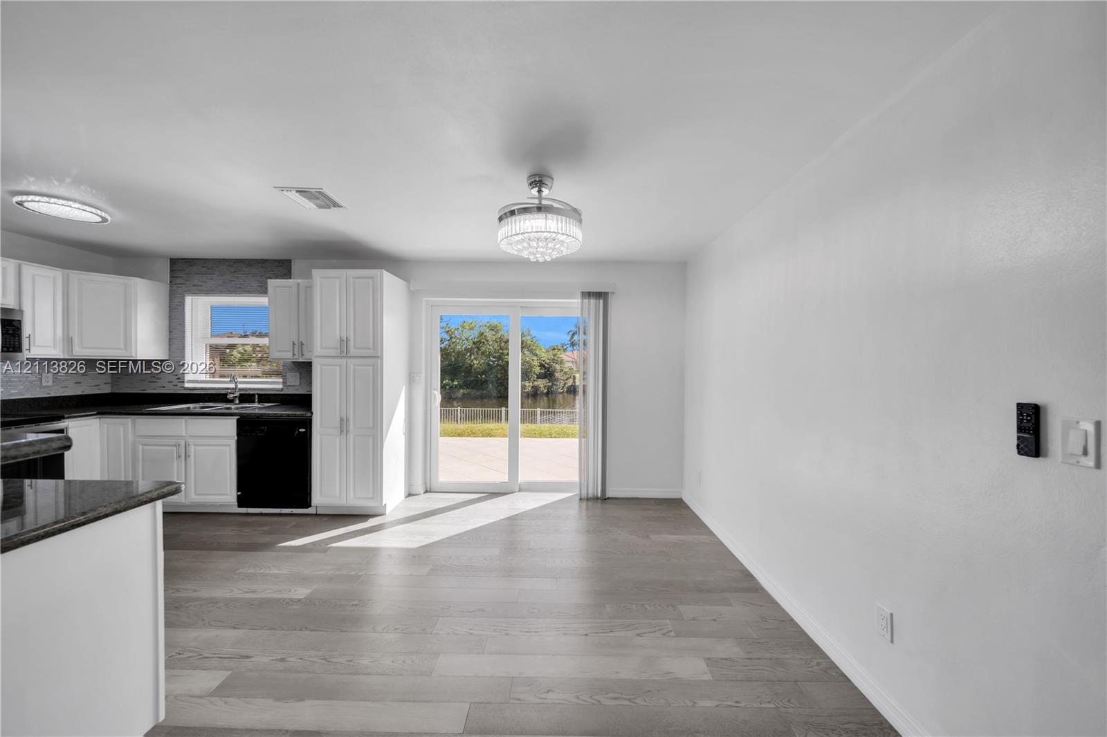 Kitchen featuring white shaker-style cabinetry, dark stone countertops, wood-finish flooring, a tiered crystal chandelier, and sliding glass doors