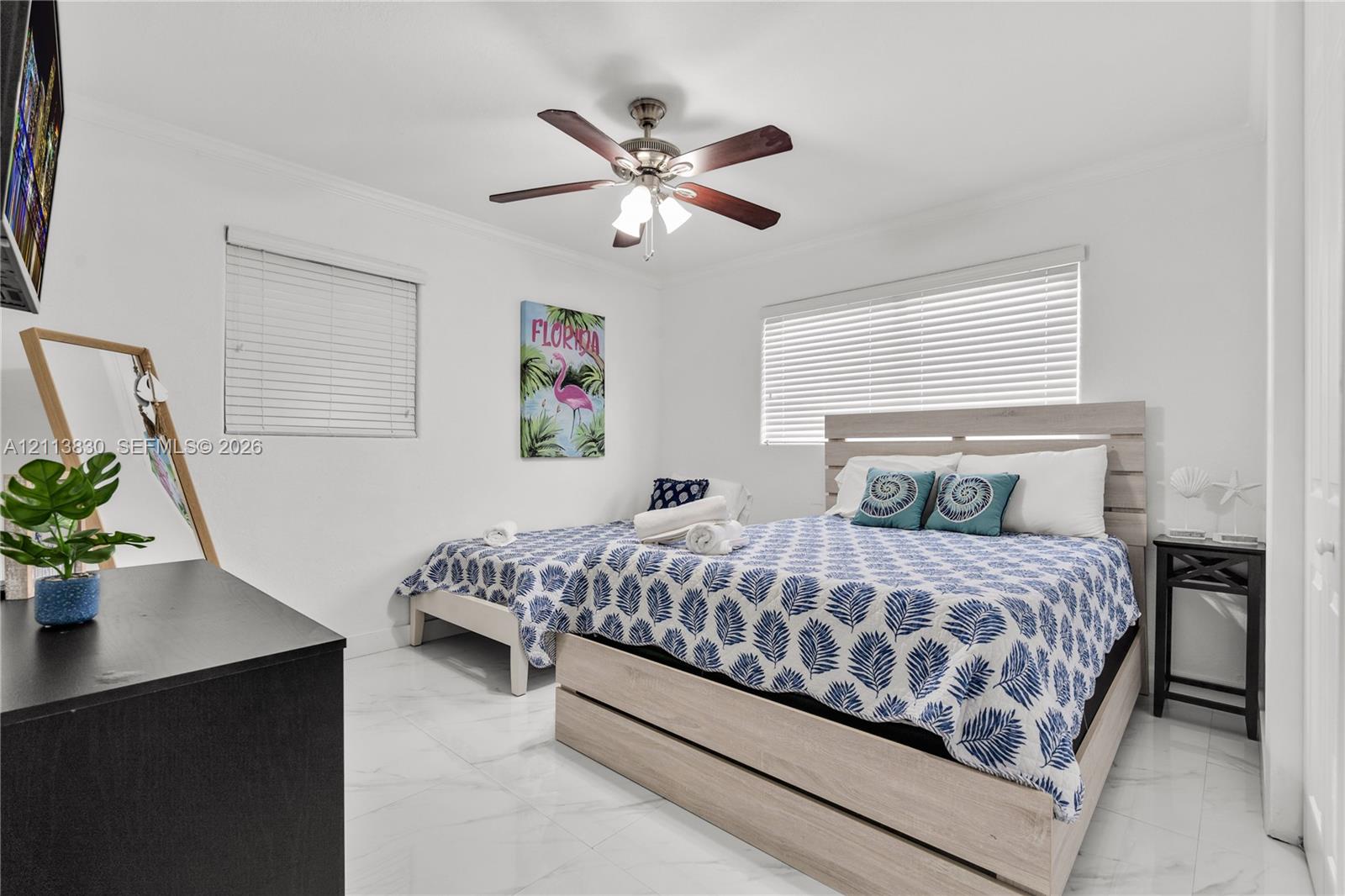 Neutral-toned interior space featuring light-colored stone-finish flooring, two large windows with horizontal blinds, and a multi-blade ceiling fan with an integrated light fixture