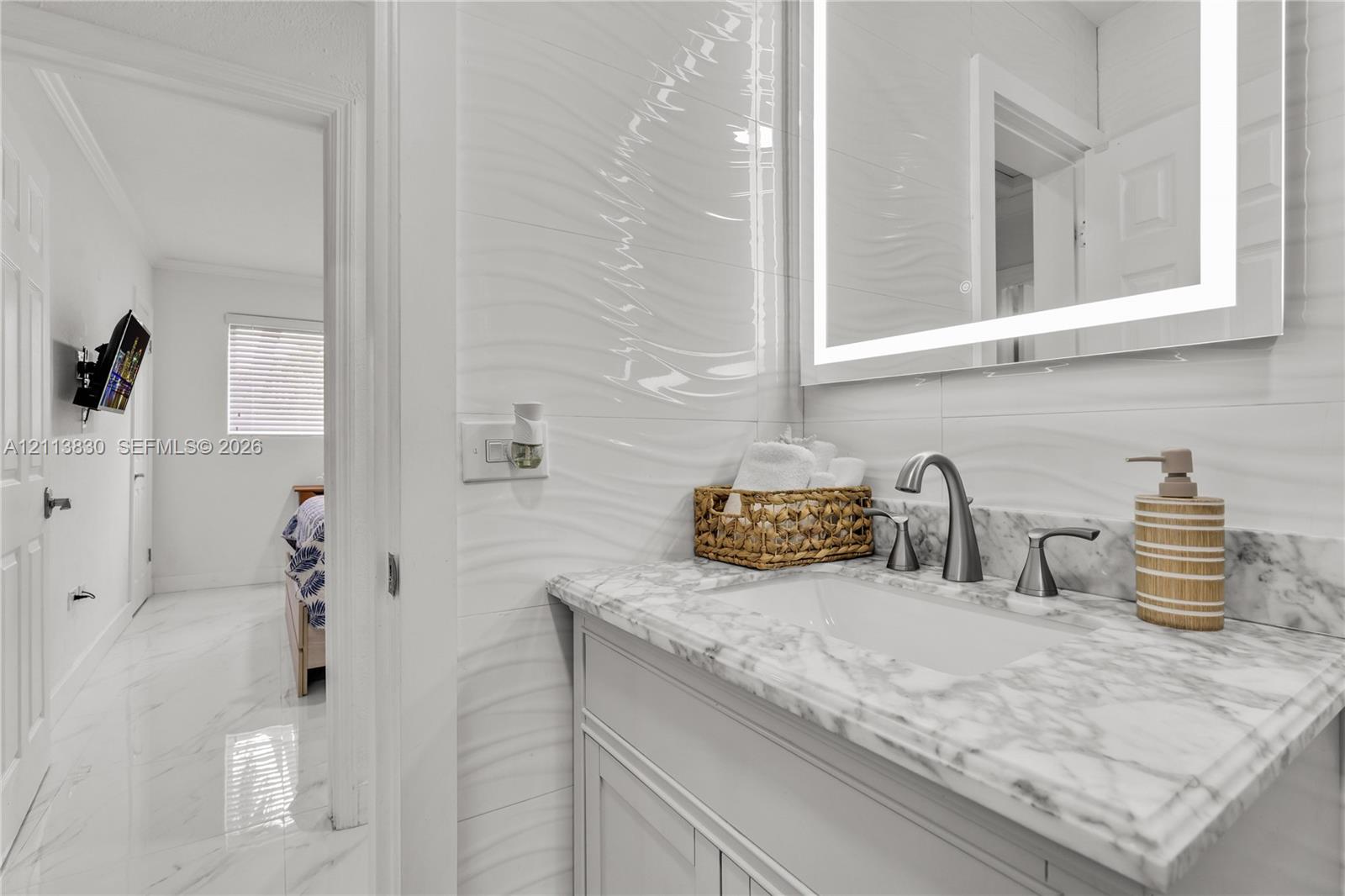Vanity featuring stone-finish countertop, undermount sink, brushed nickel faucet, integrated LED mirror, and textured wall tiling