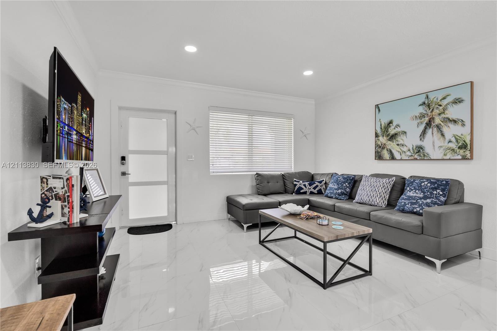 Bright living space featuring high-gloss large-format tile flooring, recessed lighting, and a frosted glass-paneled entry door