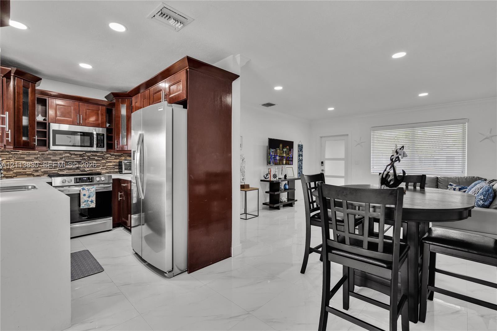 Kitchen featuring stained wood cabinetry, stainless steel appliances, multi-tonal linear tile backsplash, and white polished flooring