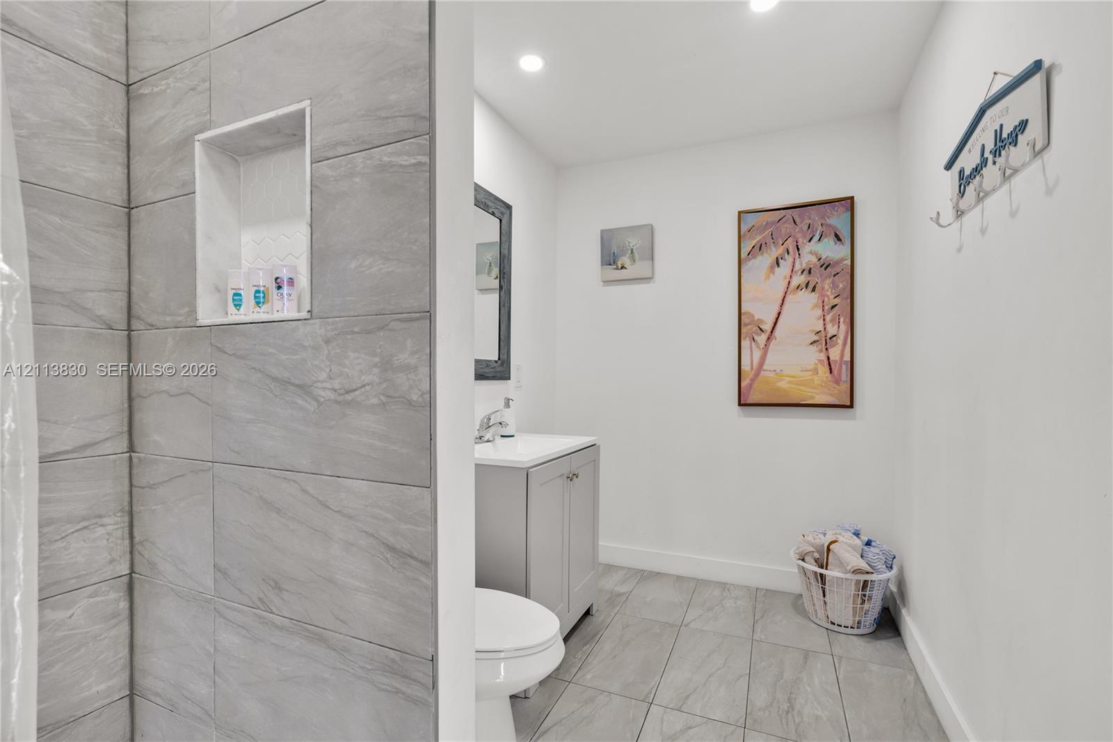 Bathroom featuring large-format grey tile shower surround with integrated wall niche, light grey vanity cabinet, solid-surface countertop, and ceramic floor tiling