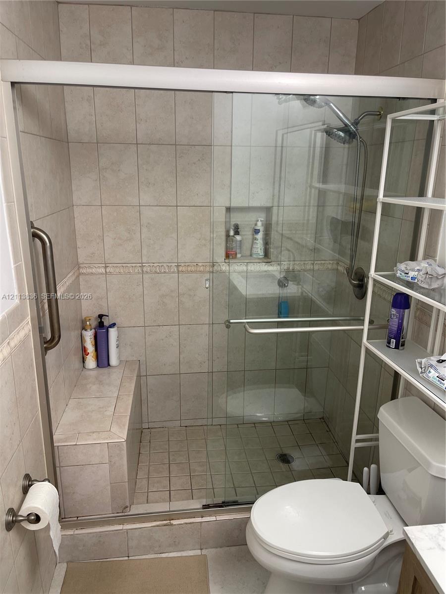 Walk-in shower featuring tile surround, integrated tiled bench, glass sliding enclosure, built-in recessed wall niche, and handheld shower fixture
