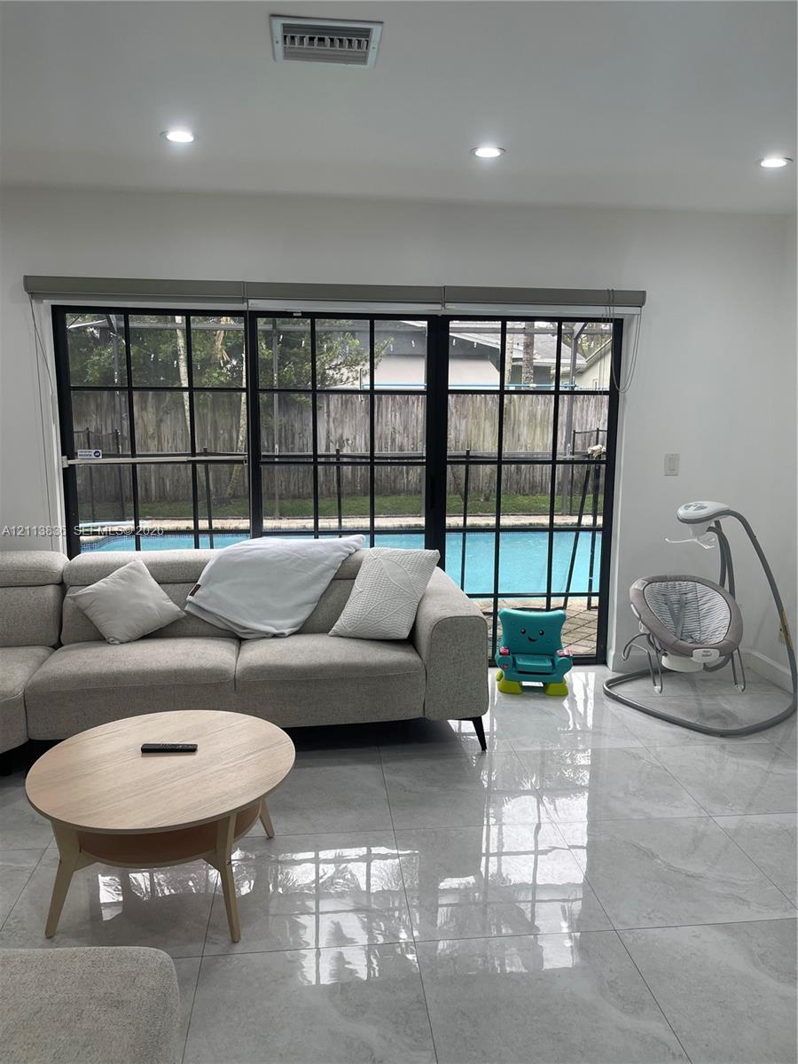 Large-format tile flooring, recessed ceiling lighting, and expansive black-framed grid windows featuring a pool exterior