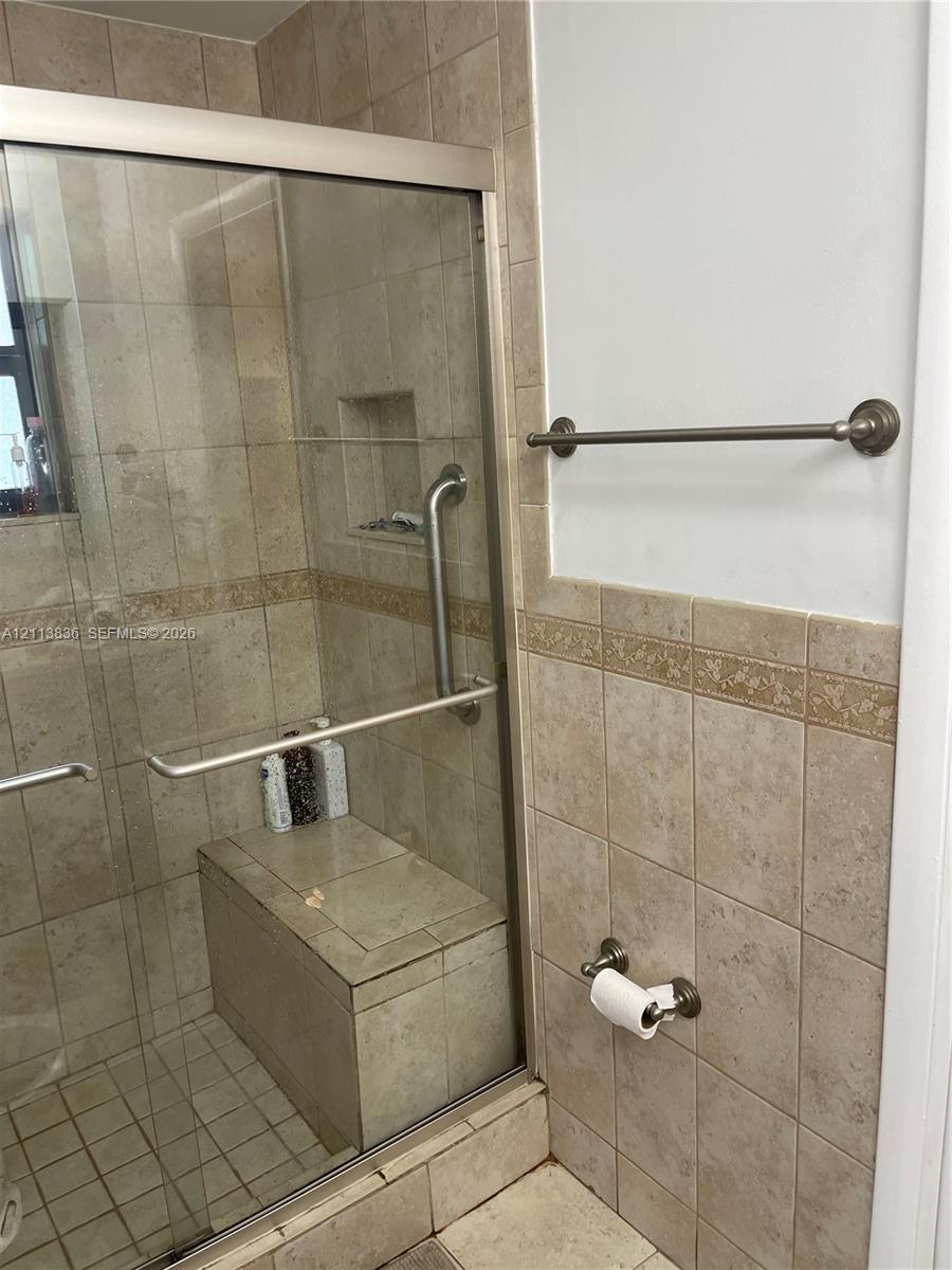 Walk-in shower featuring a tiled built-in bench, glass sliding enclosure, integrated wall niche, metal grab bar, and neutral-toned wall tiling with decorative trim
