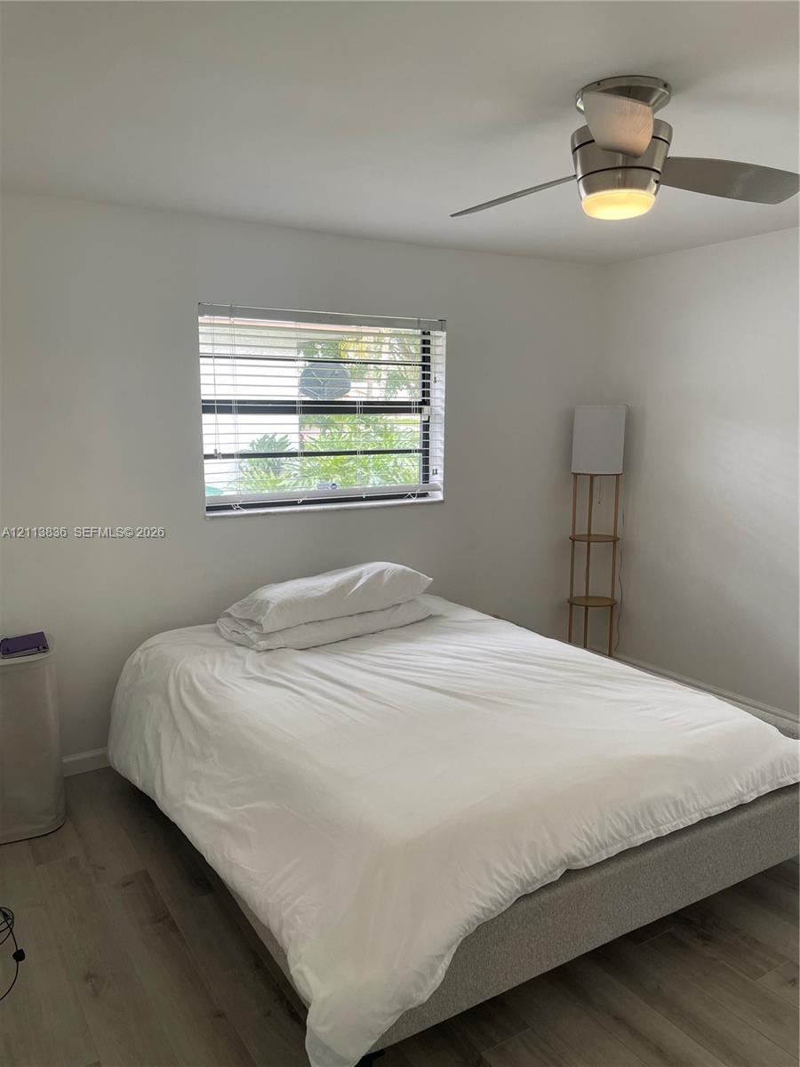 Neutral interior featuring wood-finish flooring, a horizontal window with adjustable blinds, and a ceiling-mounted fan with integrated lighting