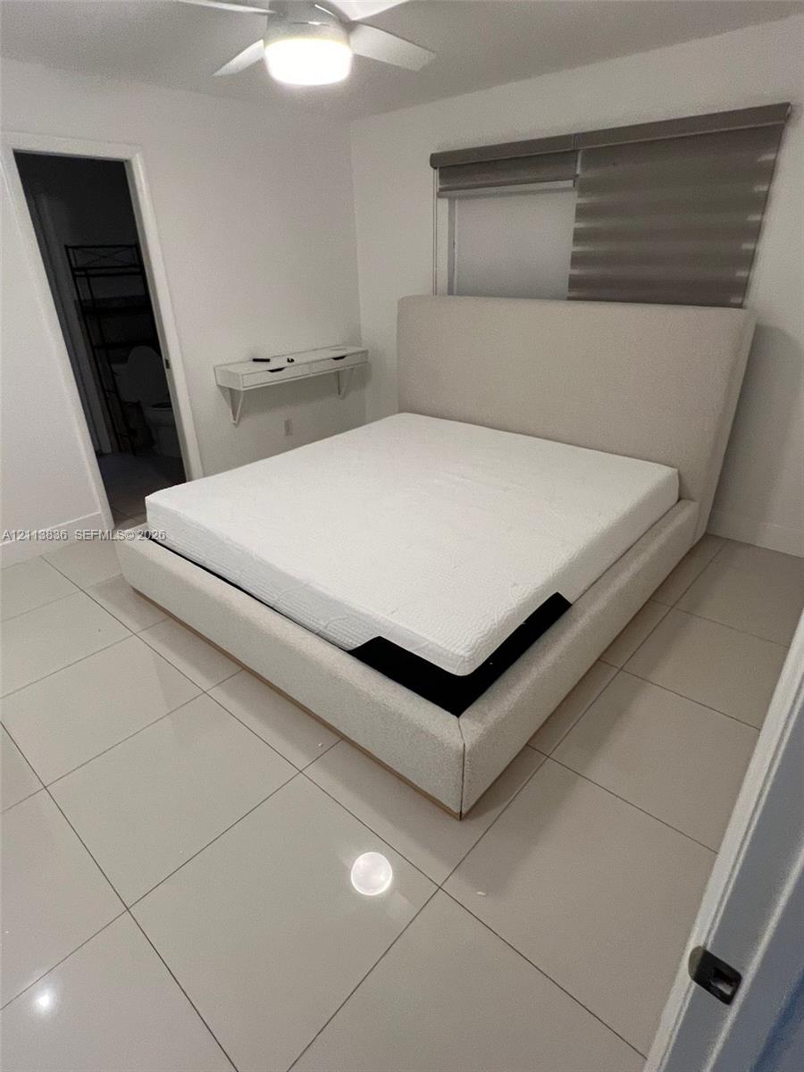 Neutral-toned tile flooring, wall-mounted floating shelf, and ceiling-mounted light fixture with an integrated fan