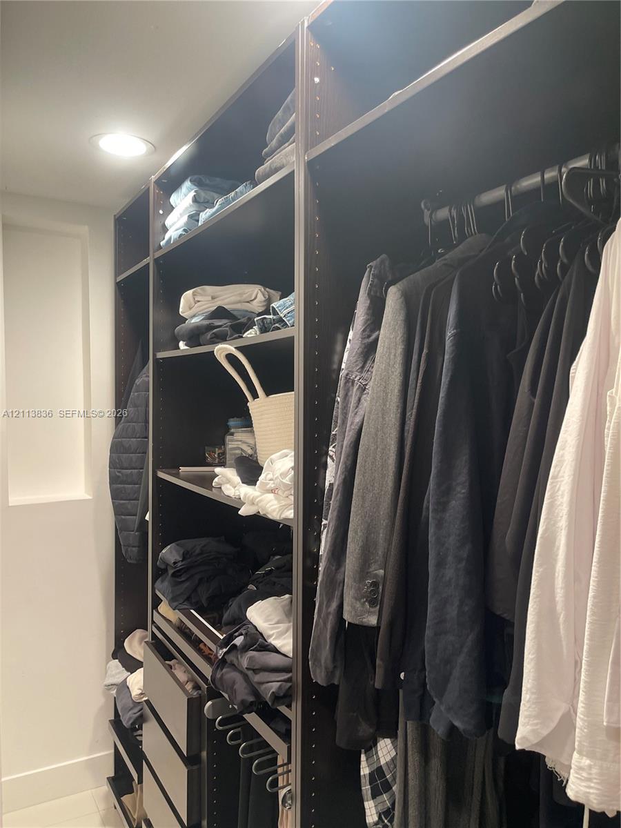Custom-built closet system featuring dark wood-finish shelving, integrated drawers, recessed lighting, and metal hanging rods