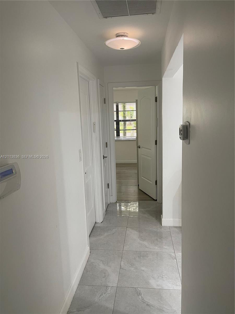 Interior hallway featuring large-format ceramic tile flooring, neutral wall finishes, semi-flush mount ceiling lighting, and multi-panel interior doors
