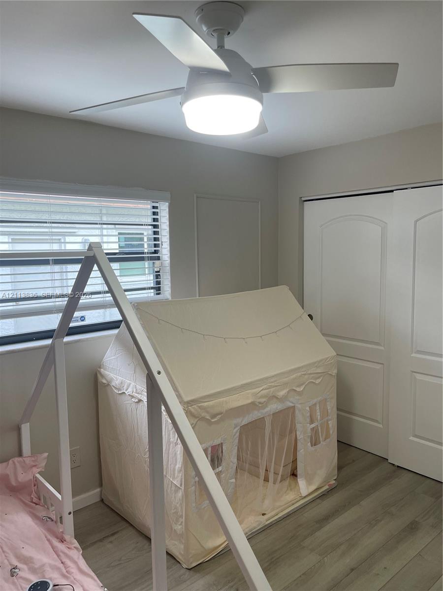 Wood-finish flooring, ceiling fan with integrated LED lighting, horizontal window blinds, and dual-panel closet doors