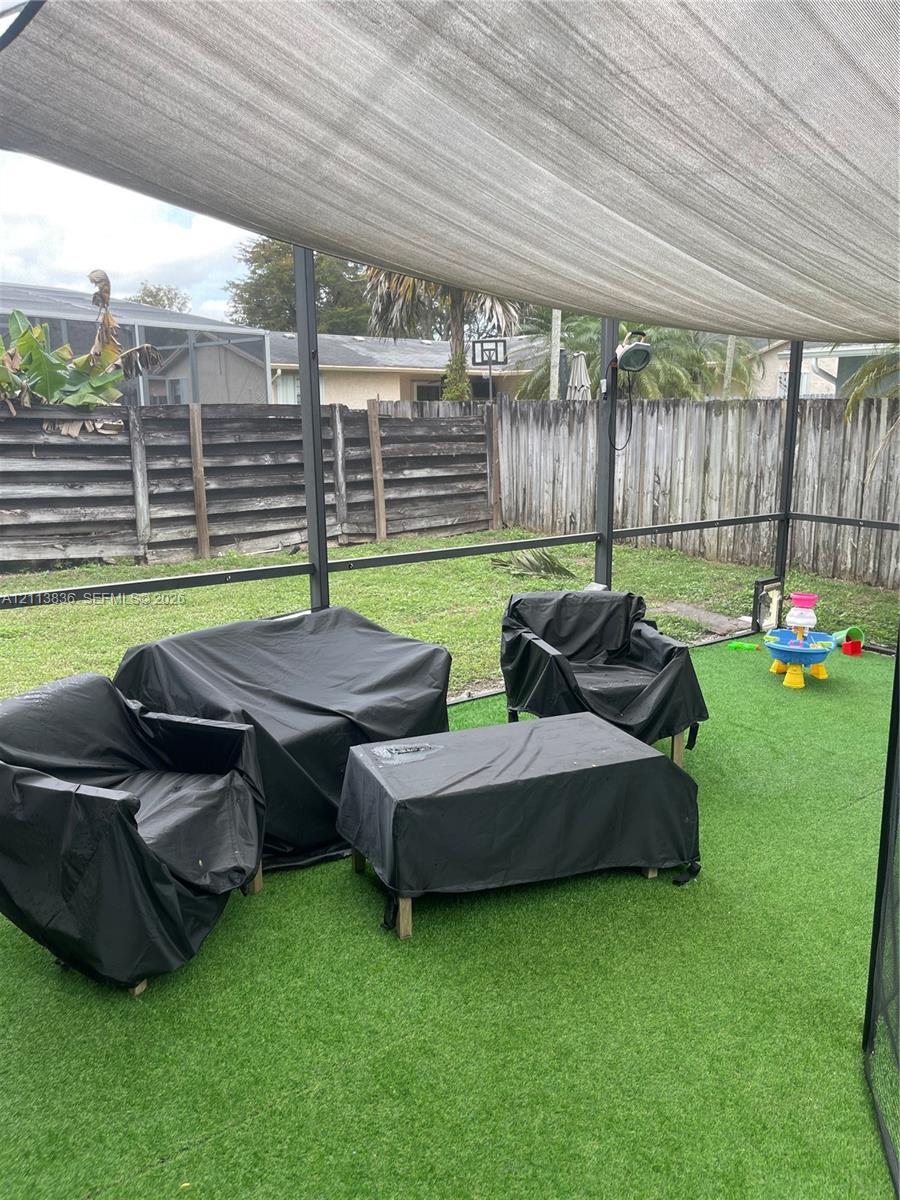 Screened-in patio featuring artificial turf, a permanent fabric sun shade, and wood-paneled privacy fencing