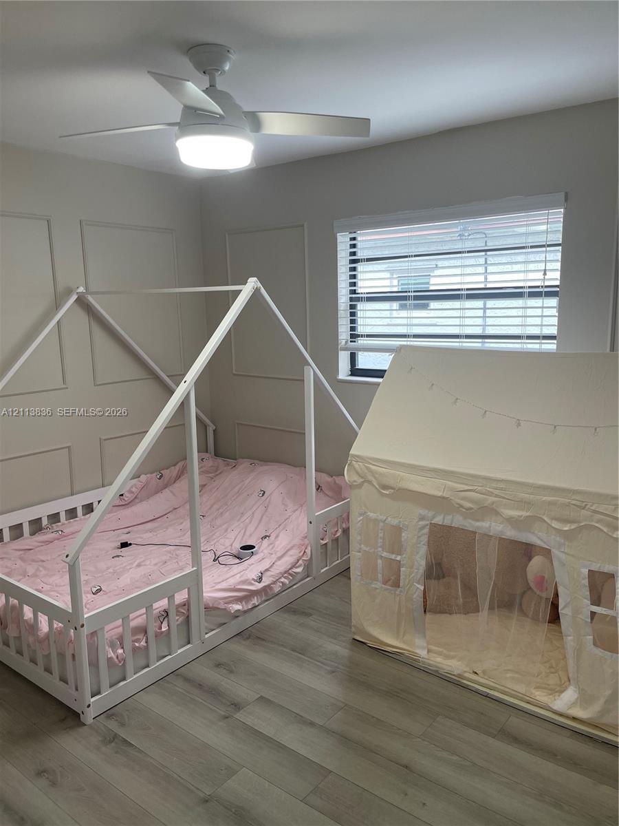 Interior room featuring wood-finish flooring, decorative wall molding, a multi-blade ceiling fan with integrated lighting, and horizontal window blinds