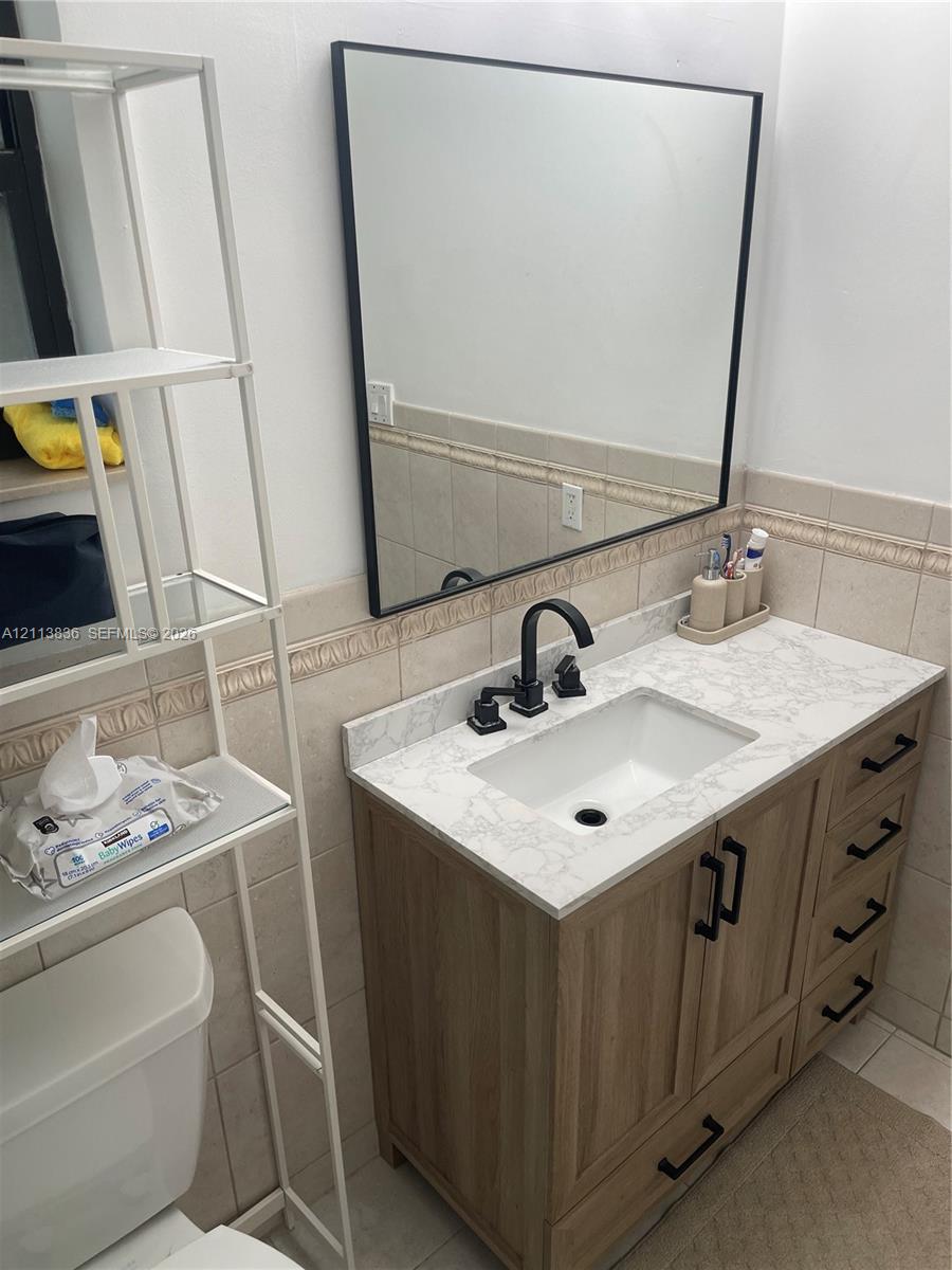 Vanity featuring wood-finish cabinetry, a stone-patterned countertop, integrated basin, matte black faucet, and a rectangular mirror with a black frame